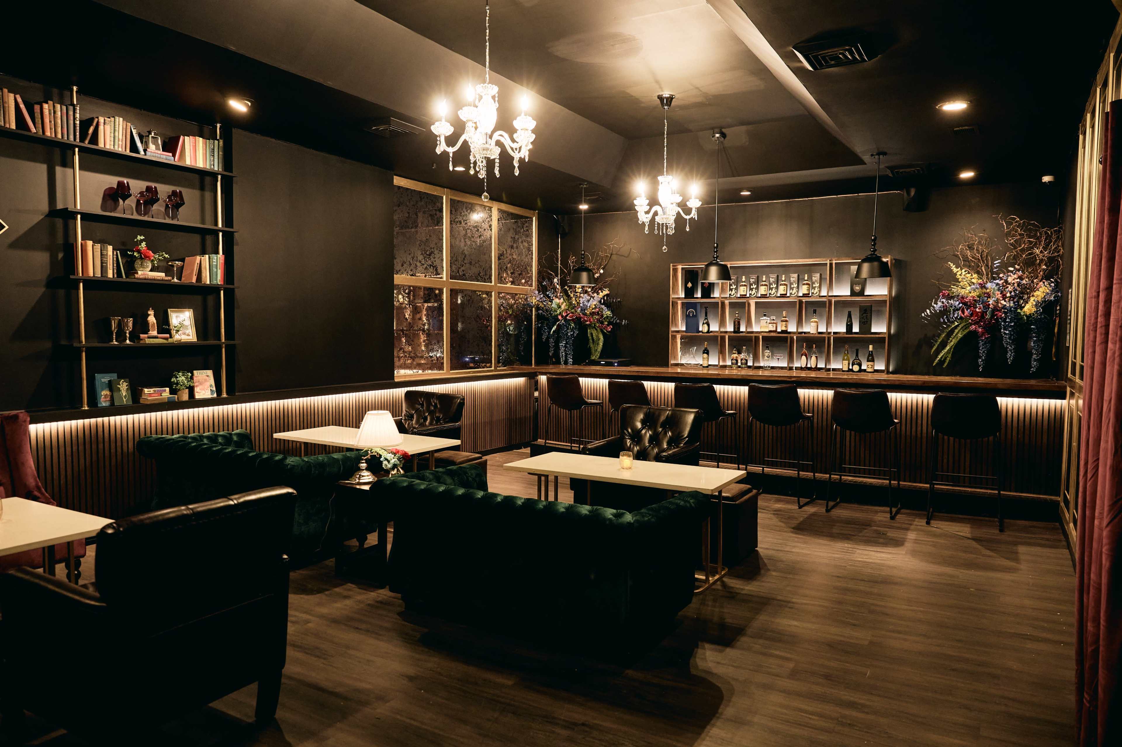 A cozy lounge with dark walls, stylish seating, shelves of books, and a well-lit bar area.