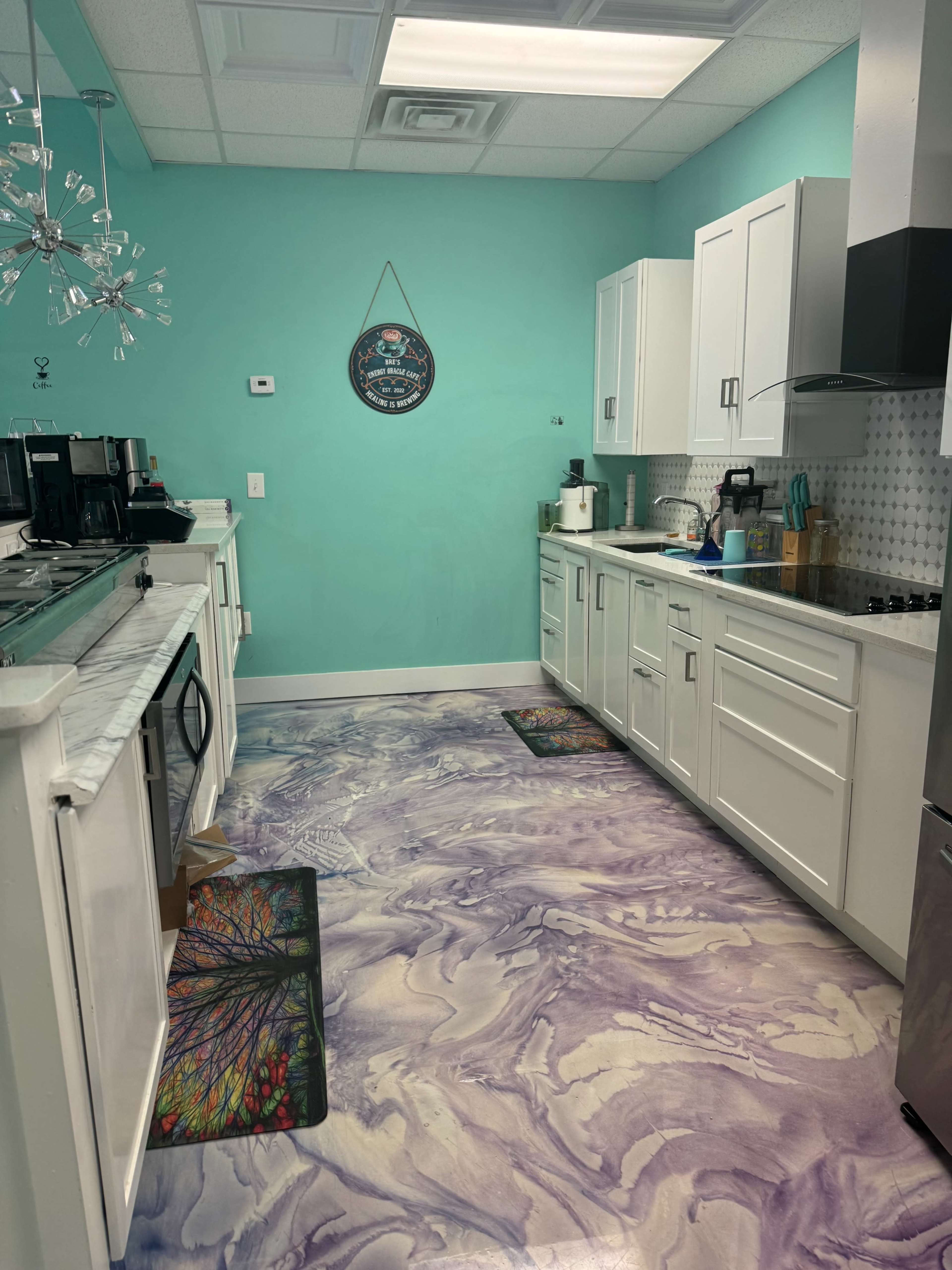 A modern kitchen with white cabinets, a marble countertop, and a vibrant turquoise wall, featuring a colorful, marbled floor design.