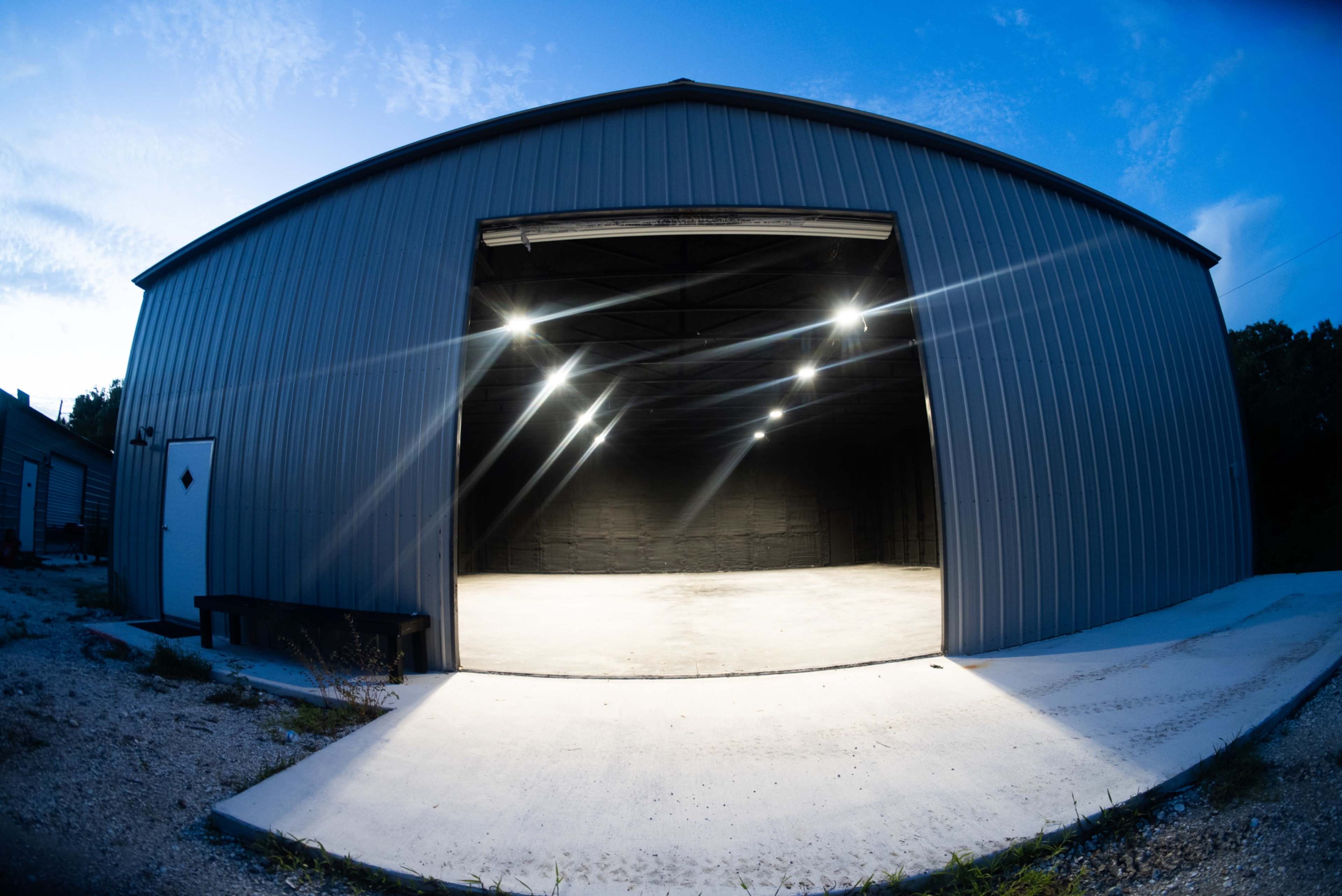 A large metal building with an open entrance, illuminated by overhead lights, and a concrete surface outside.