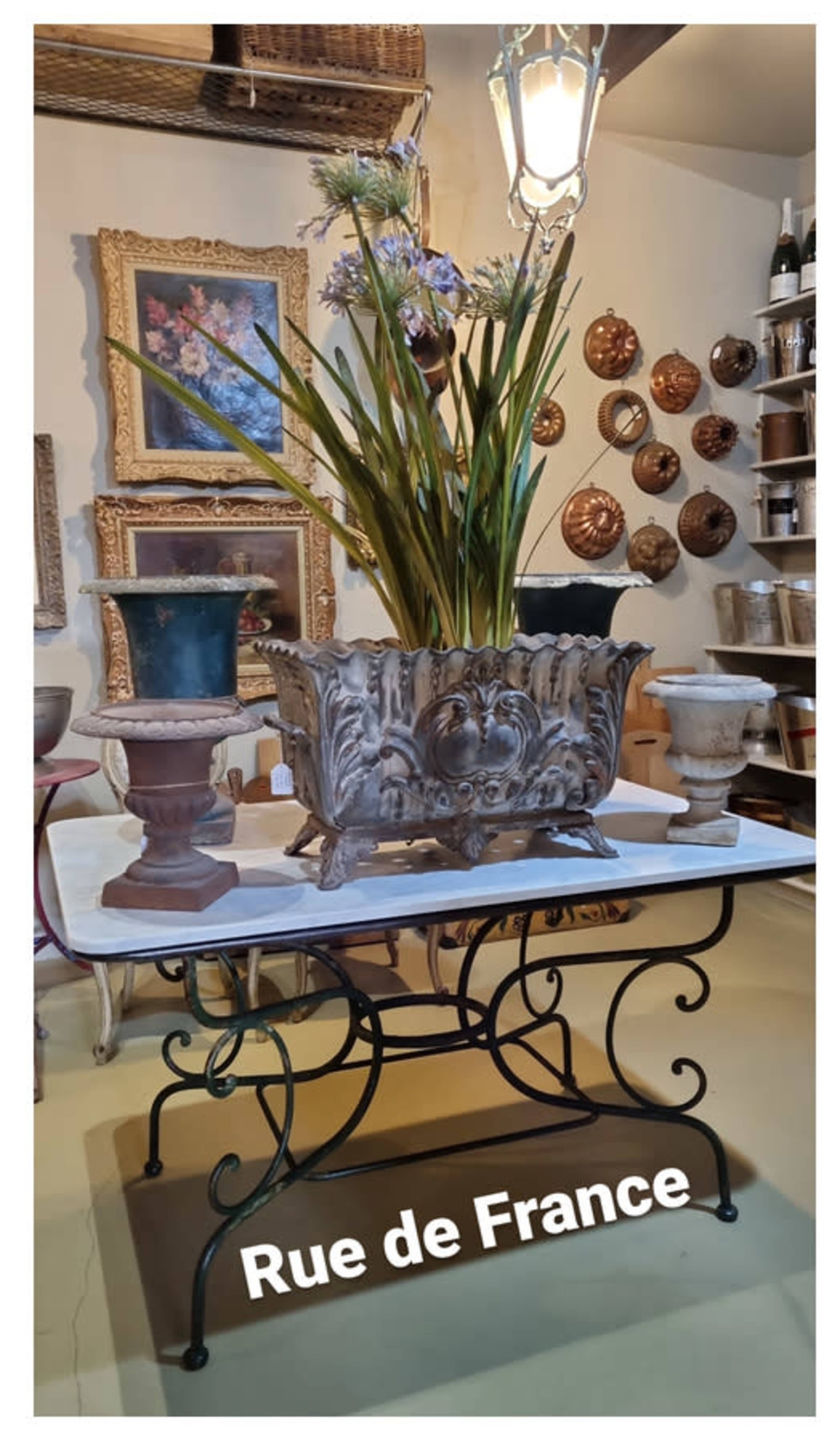 A decorative table displays a vintage planter with flowers, surrounded by various pottery and framed artworks in a shop labeled "Rue de France."