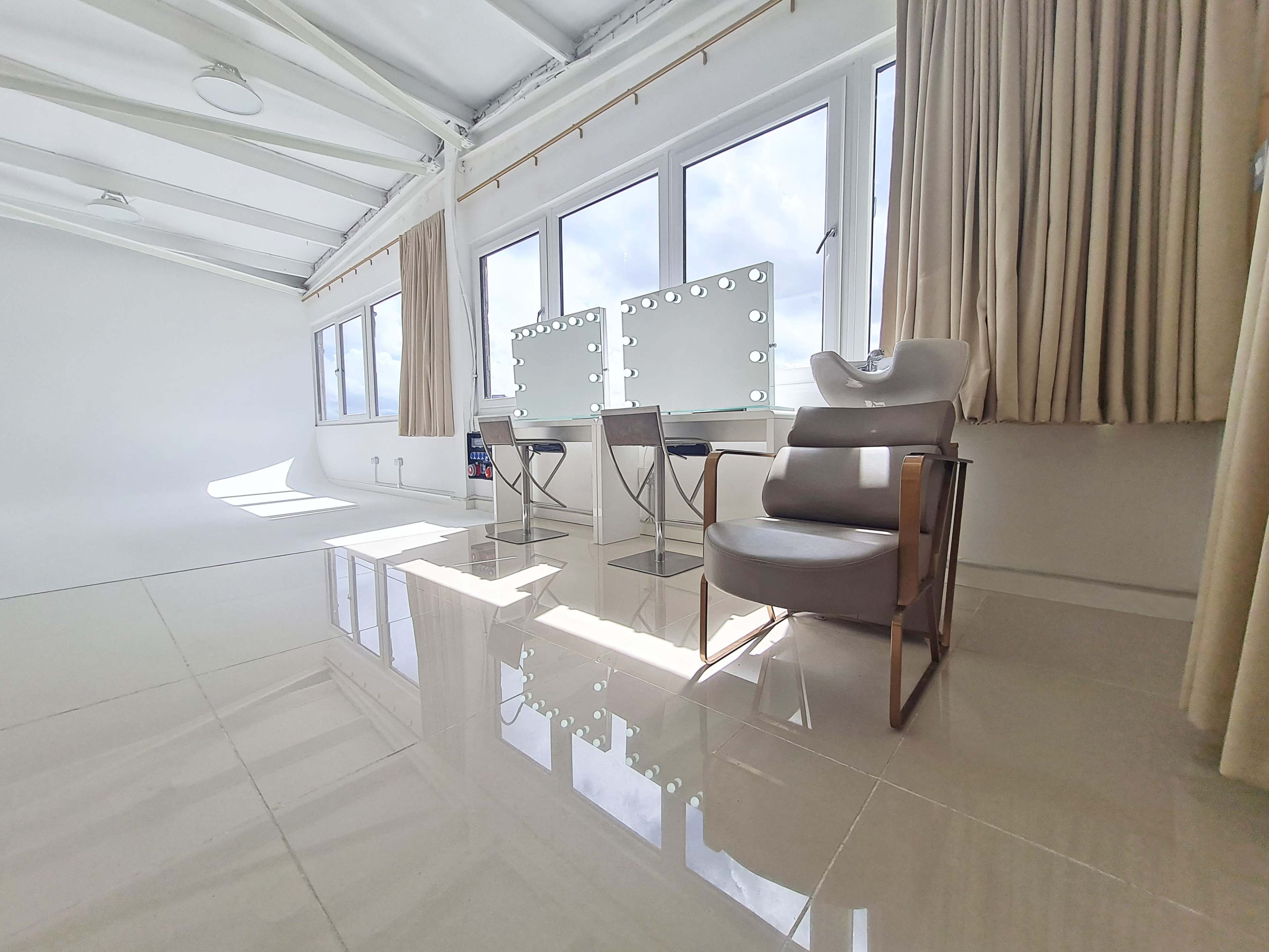 A bright, modern interior with large windows, two vanity mirrors, and a stylish chair.