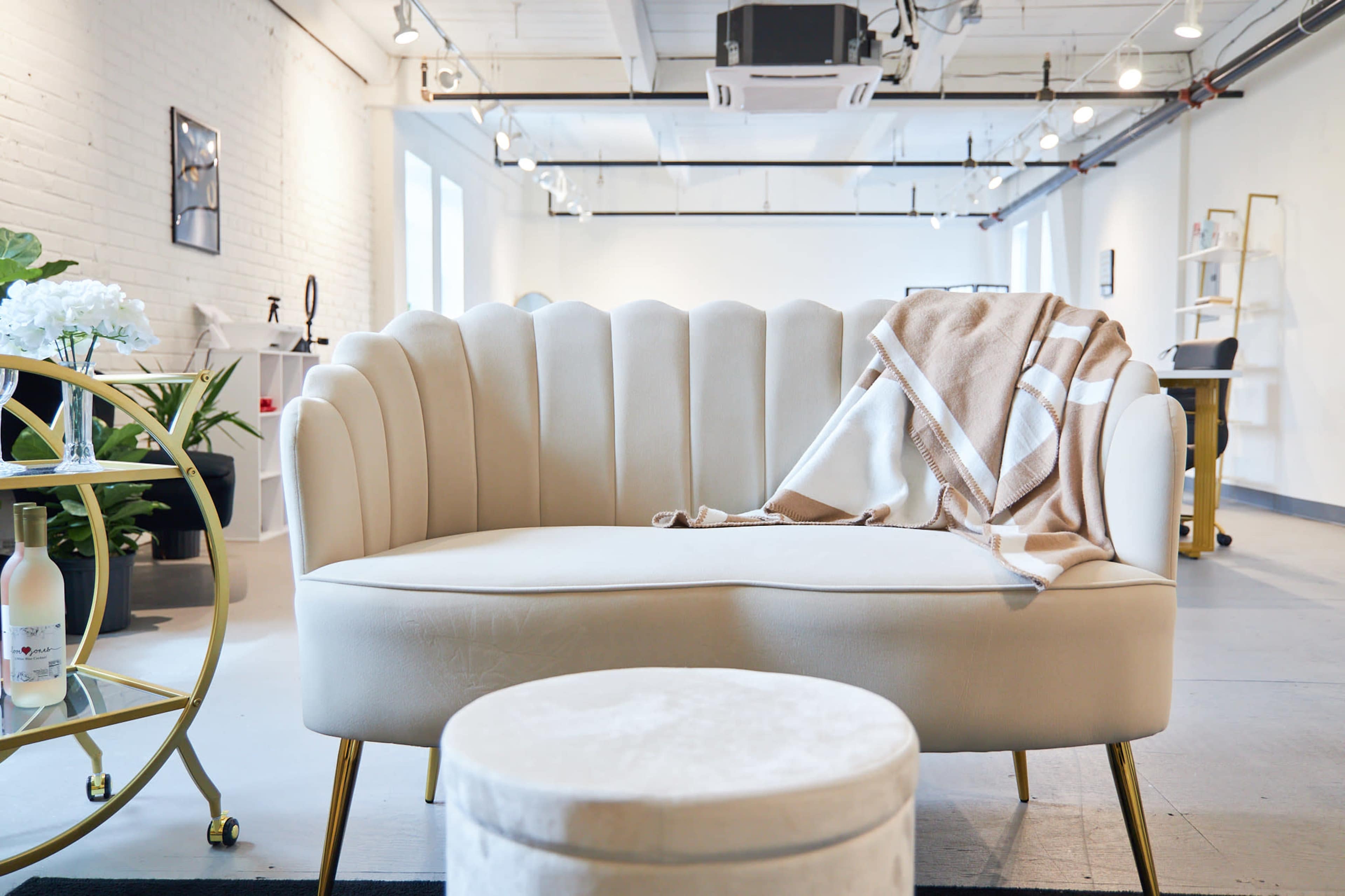 A modern, stylish seating area featuring a cream-colored scalloped sofa with a throw blanket draped over it, accompanied by a round ottoman and a small side table.