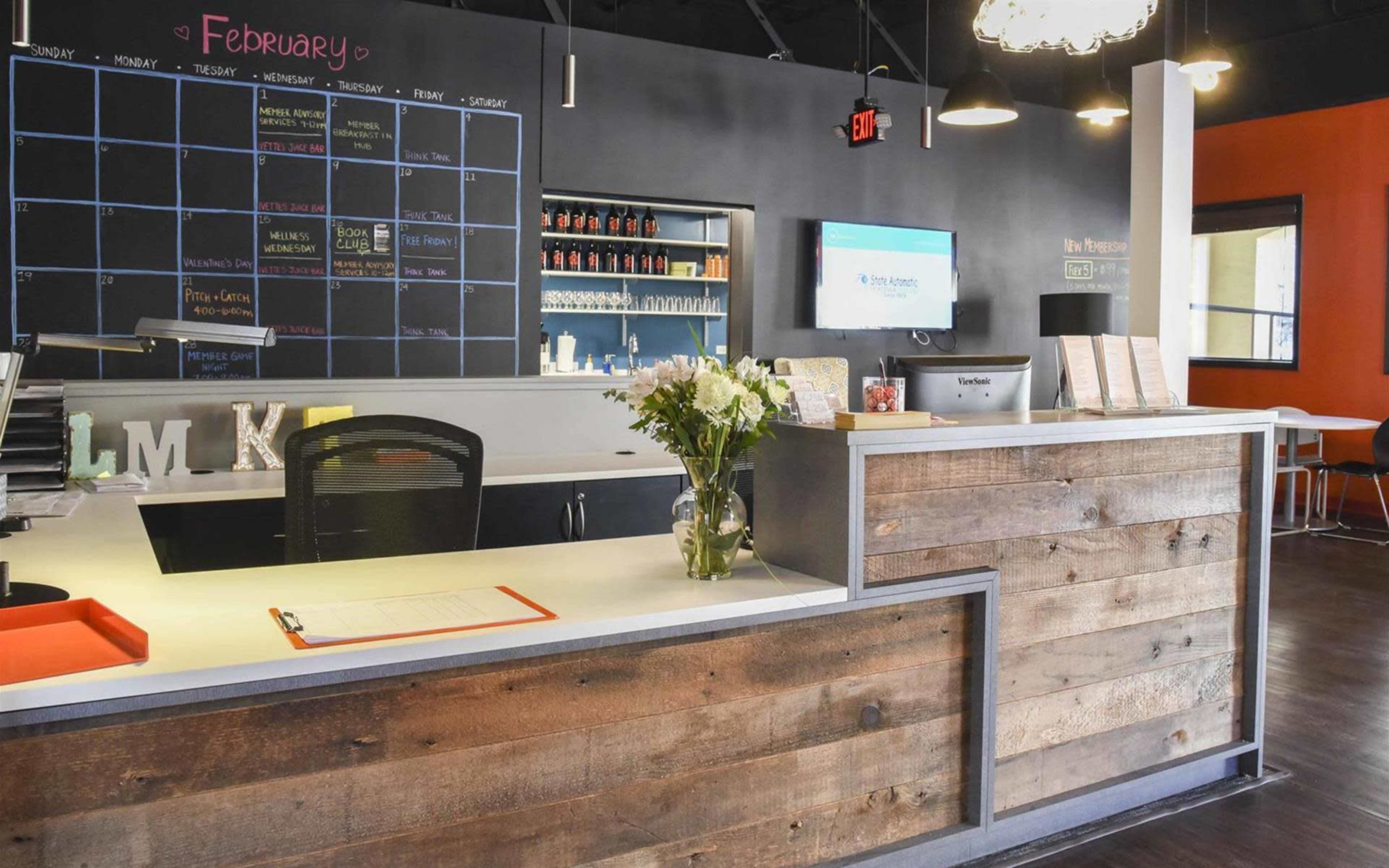 A reception area with a wooden front desk, a wall calendar for February, and a digital screen displaying information.