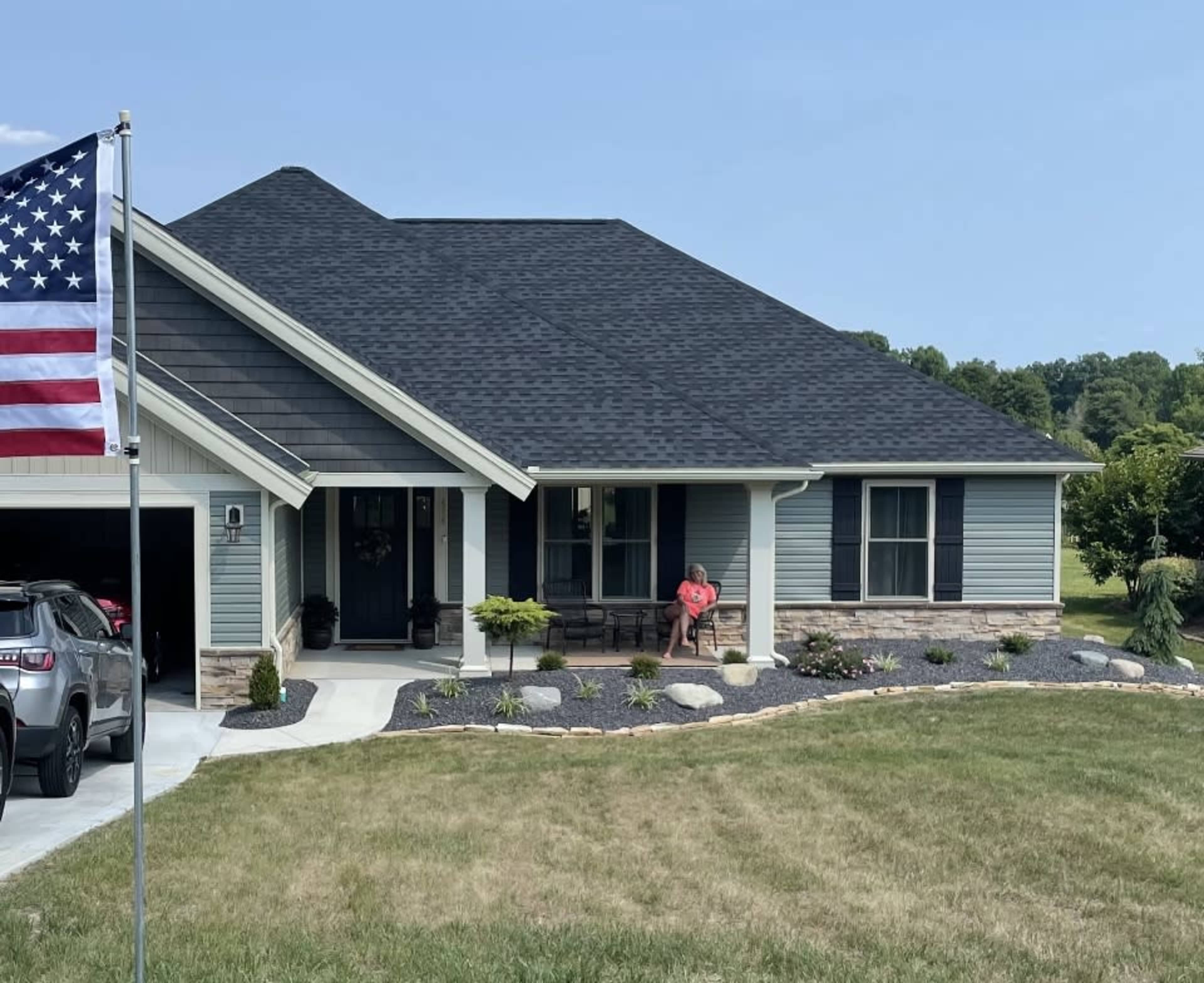 A modern house with a blue exterior features a well-maintained front yard and a large American flag flying in the foreground.