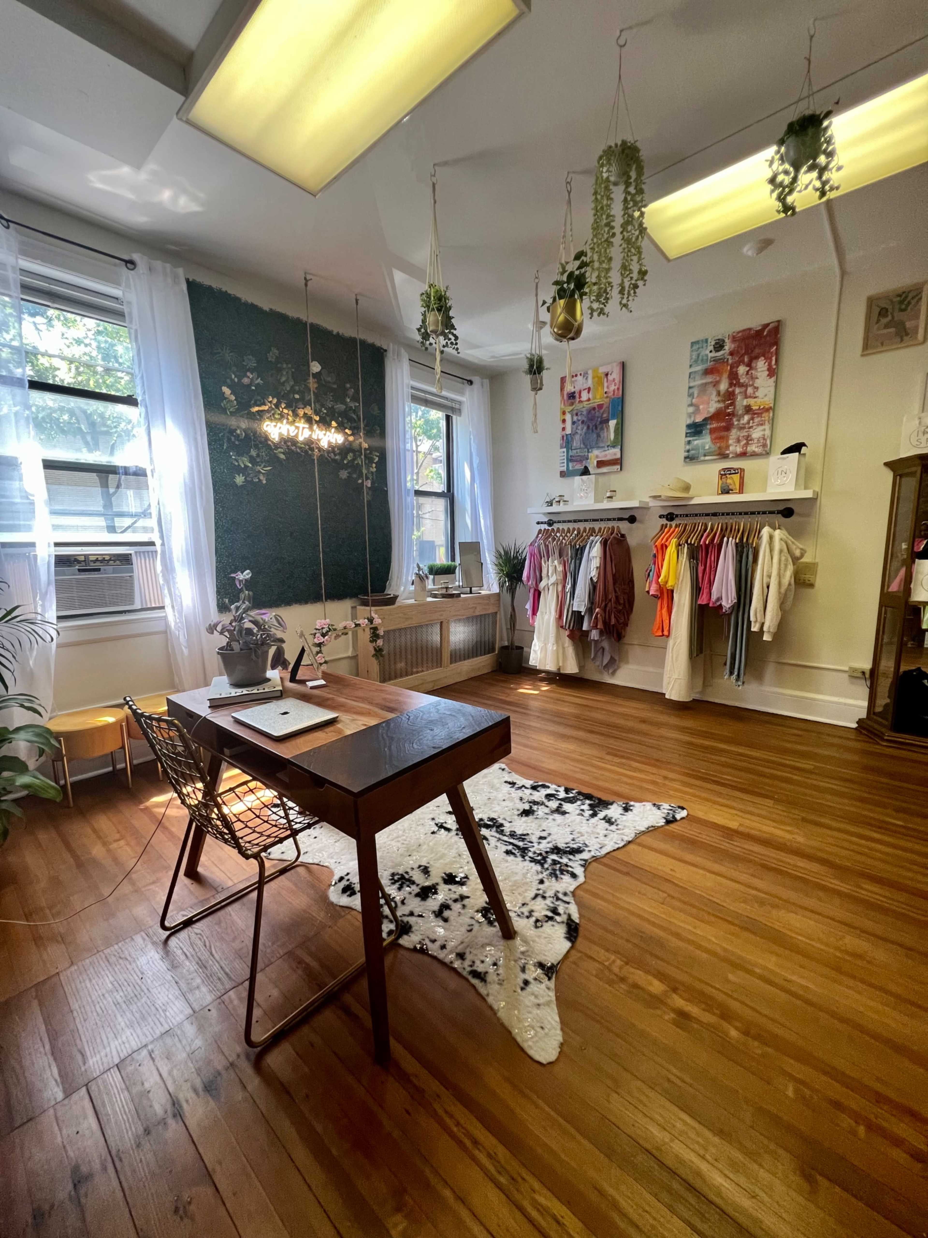 A bright, organized room with a wooden desk, a rug on the floor, and clothing arranged on racks against the wall.