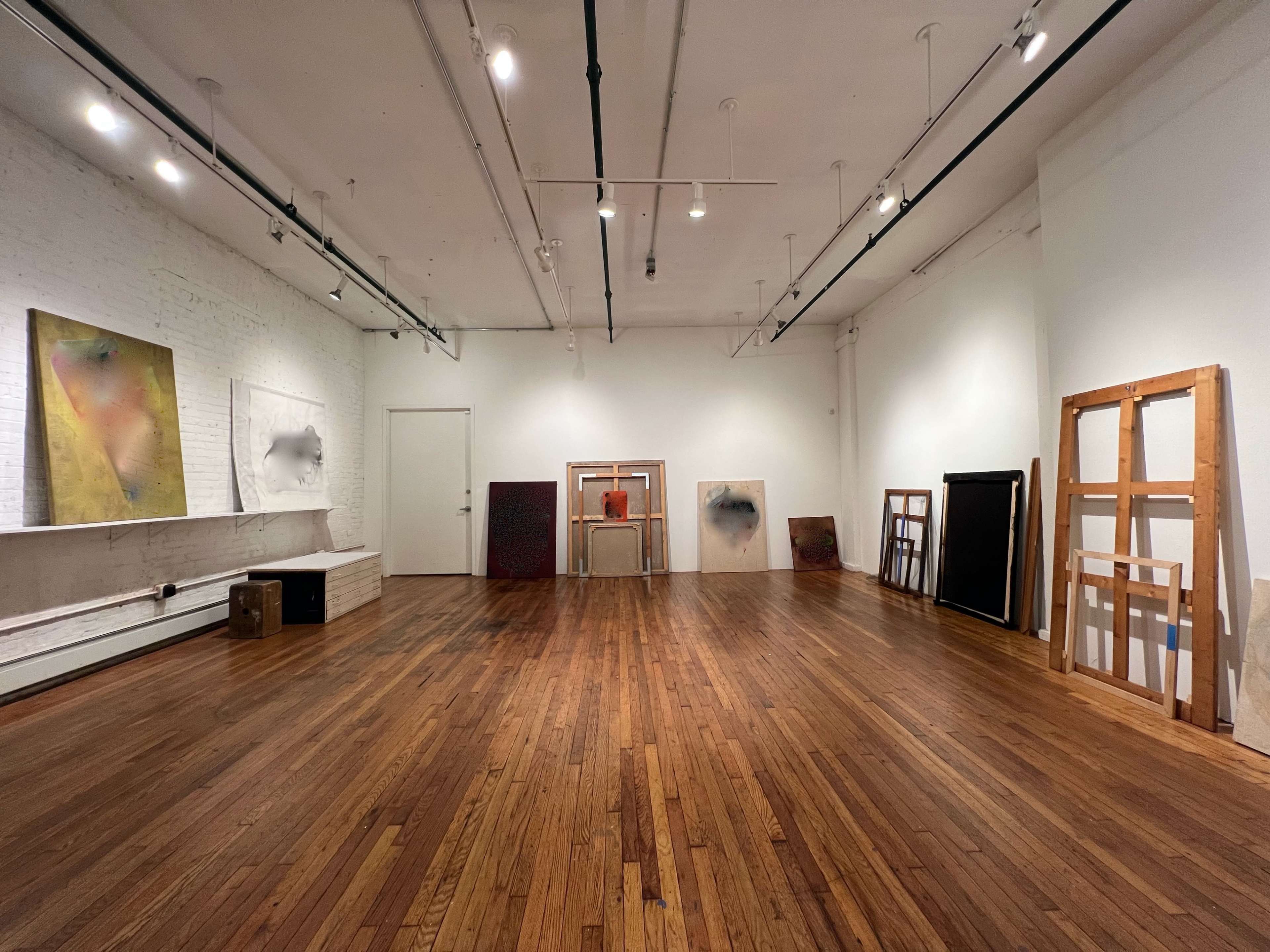 A spacious art gallery with wooden flooring, featuring several framed artworks displayed around the room.