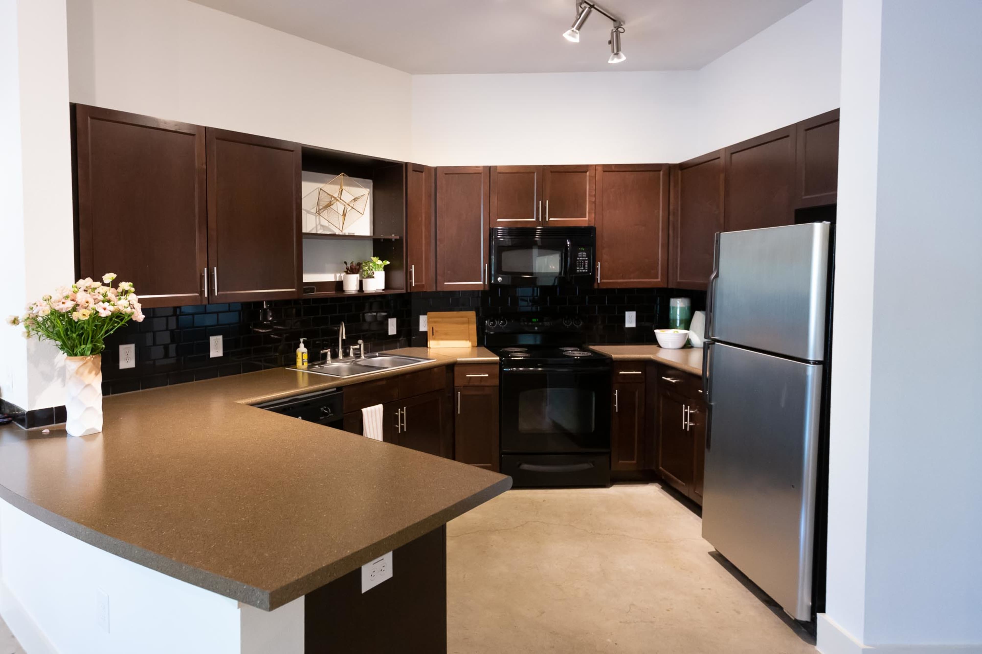 A modern kitchen with dark wooden cabinets, black appliances, and a light-colored countertop.