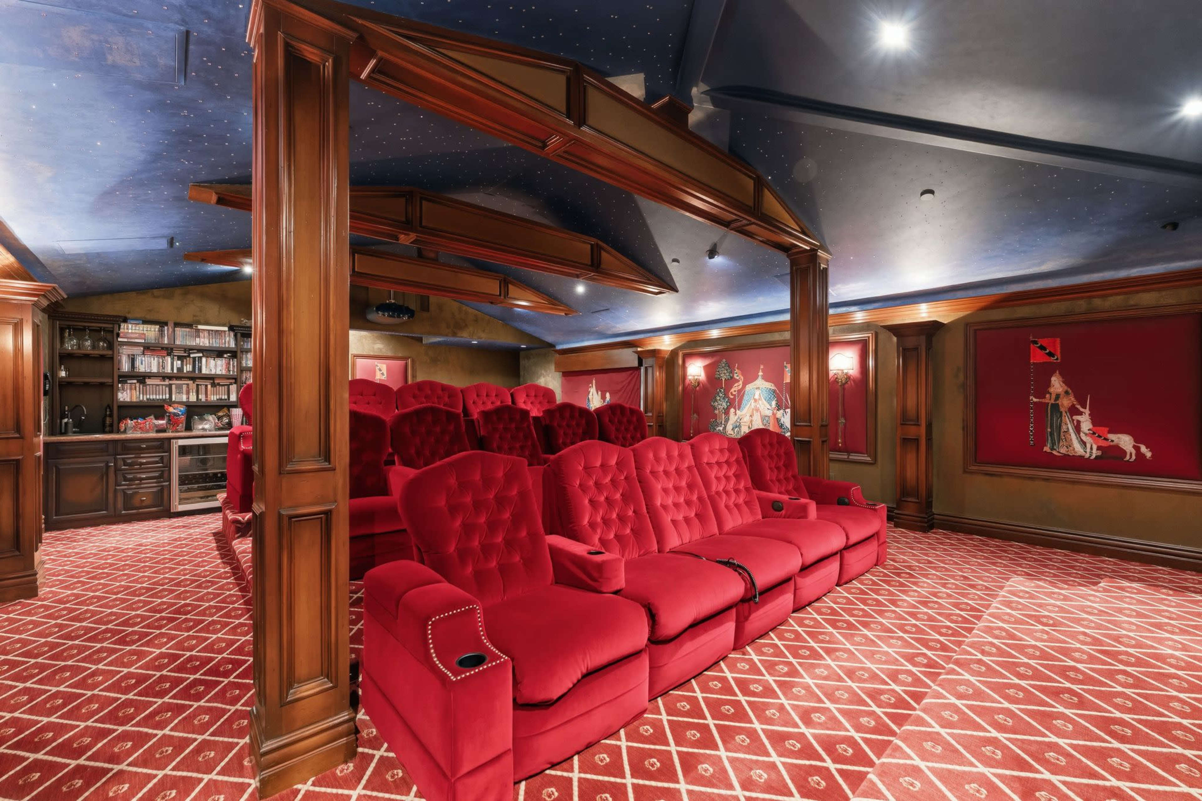 The image shows a luxurious home theater with red velvet seating arranged in a tiered layout and a wooden bar area in the background.