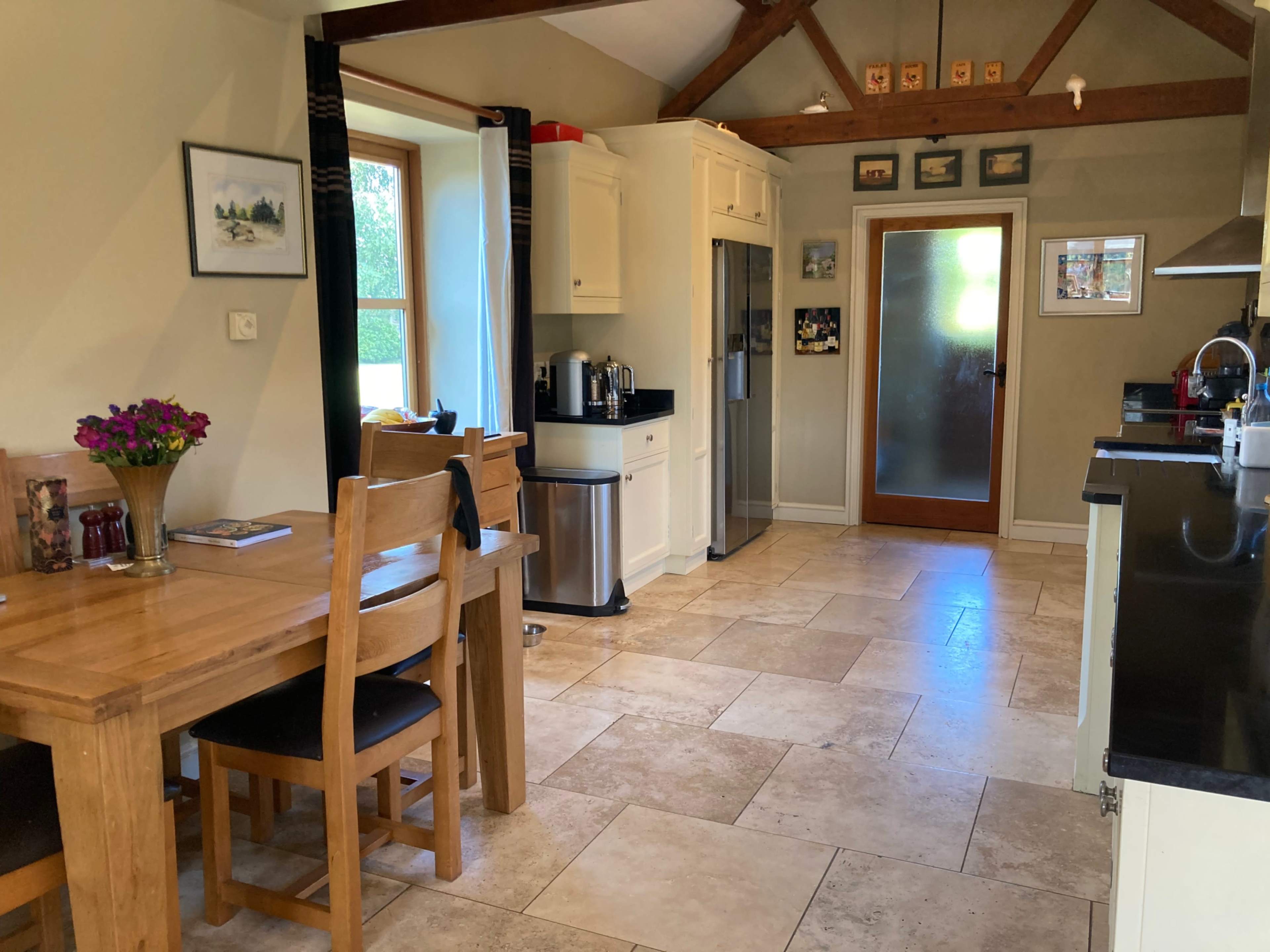 A spacious kitchen with a dining table, black countertops, a refrigerator, and a glass door leading to the outside.