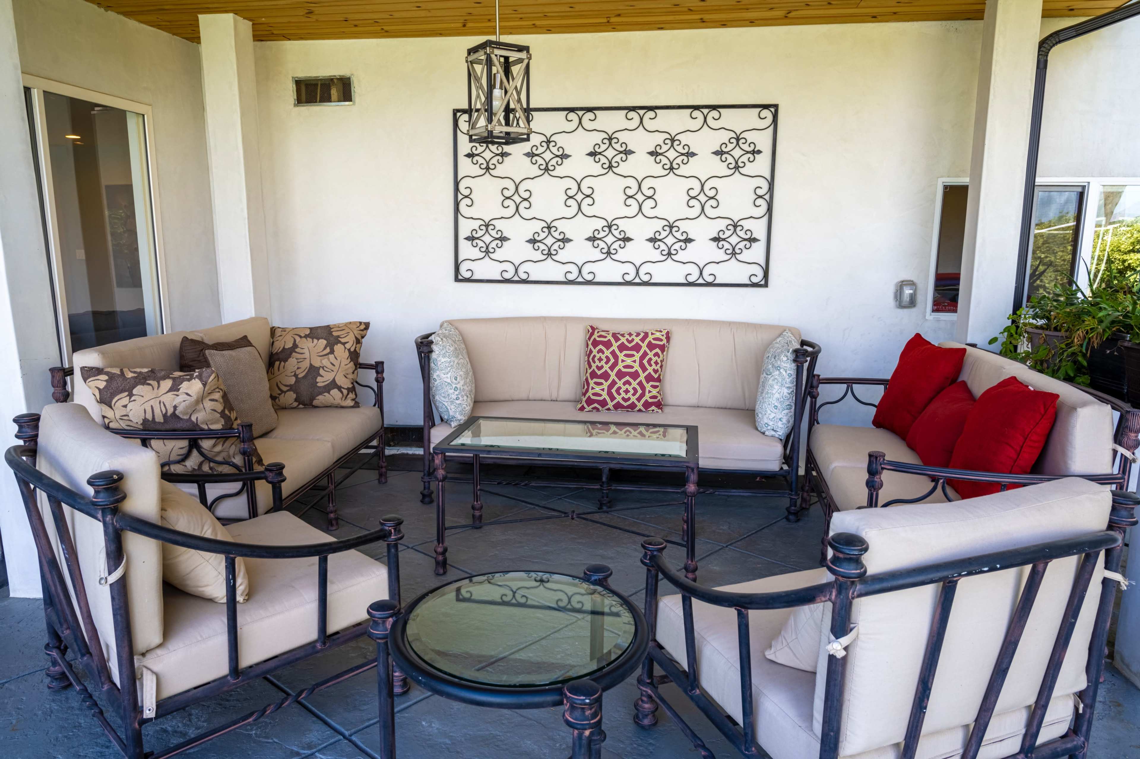 A seating area features a glass coffee table surrounded by beige couches with decorative pillows and a wrought iron wall hanging.