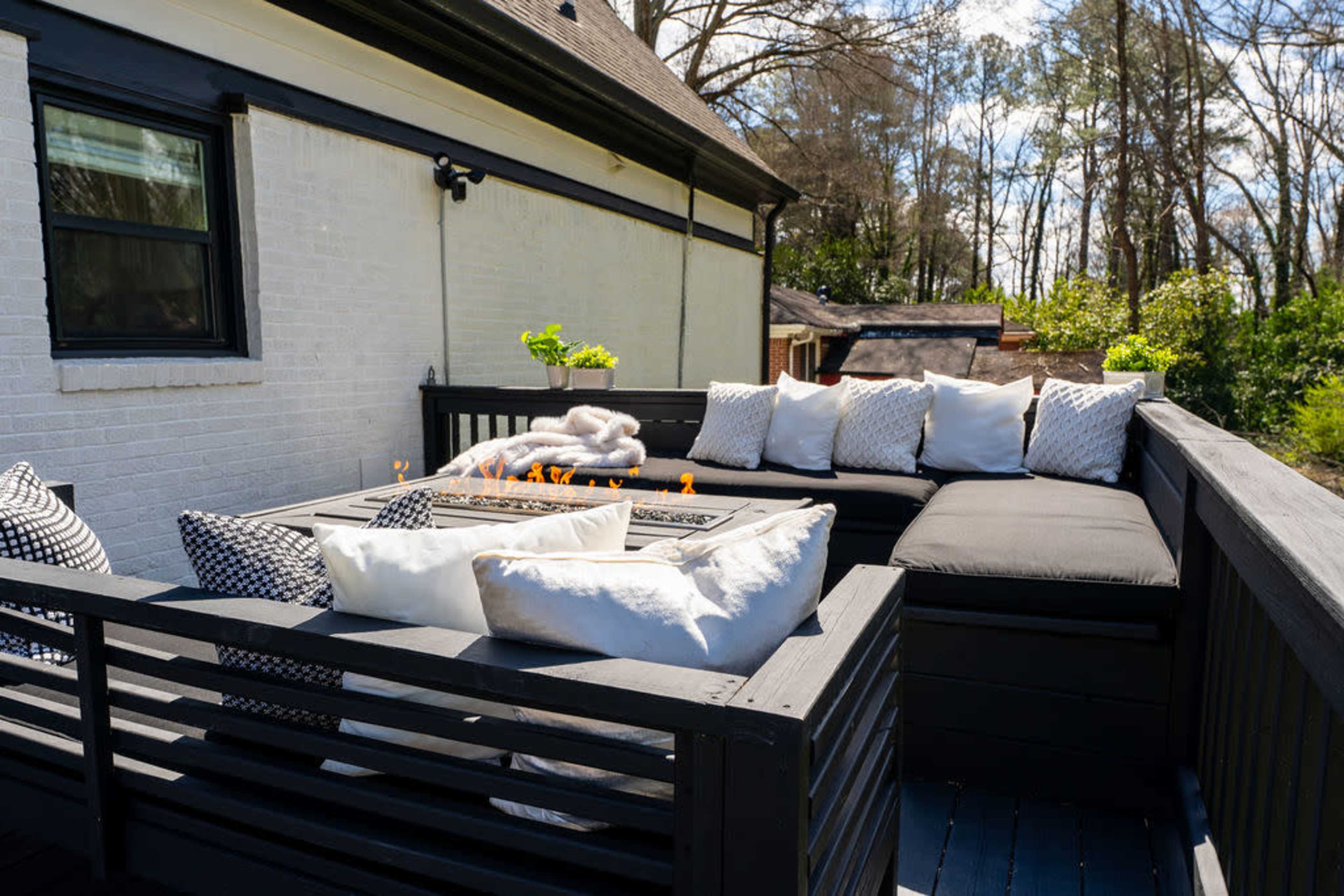 A modern outdoor seating area features a fire pit surrounded by plush cushions on a wooden deck.