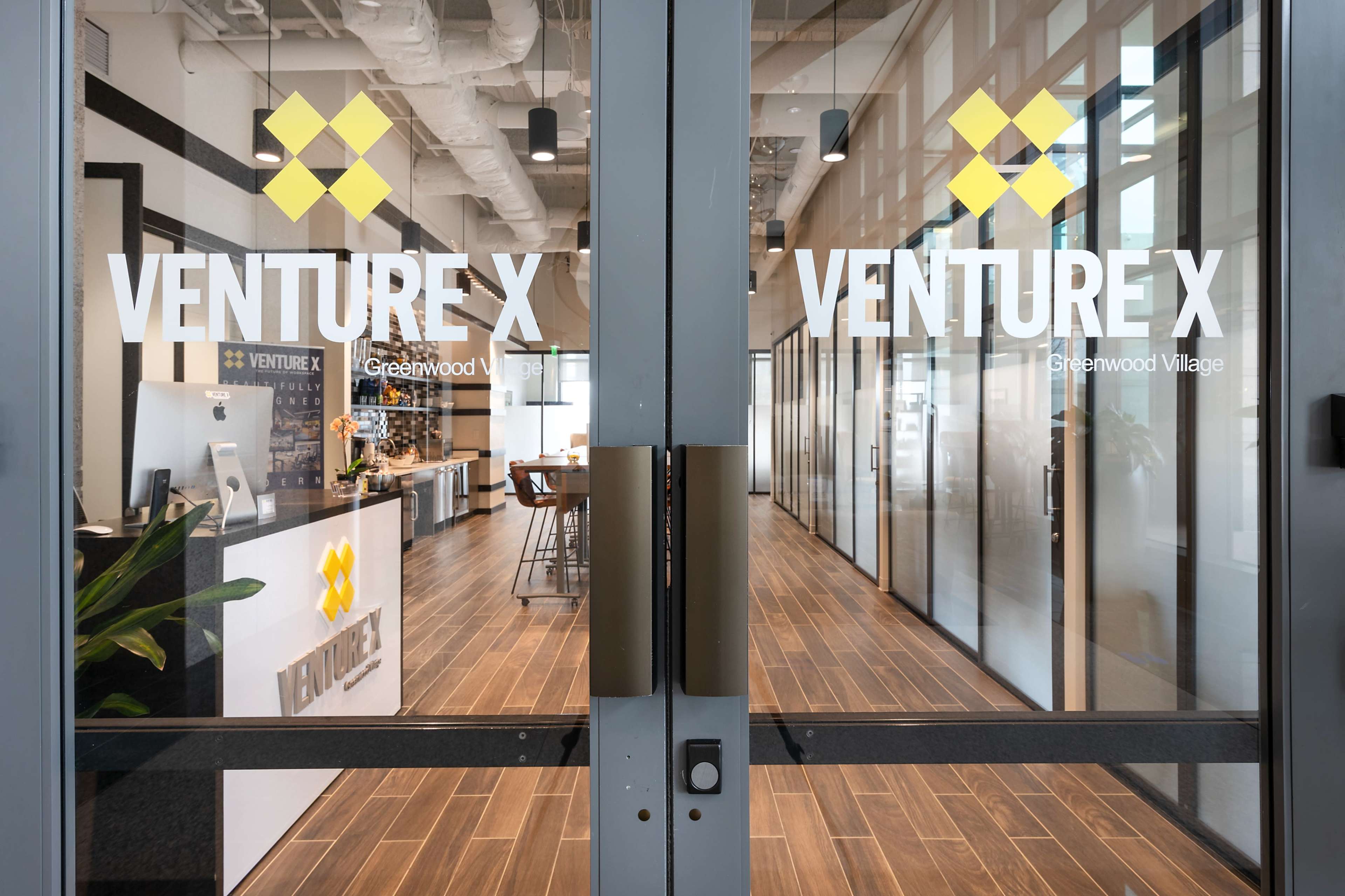 The entrance of a modern office space with glass doors labeled "VENTURE X" and a reception area visible inside.