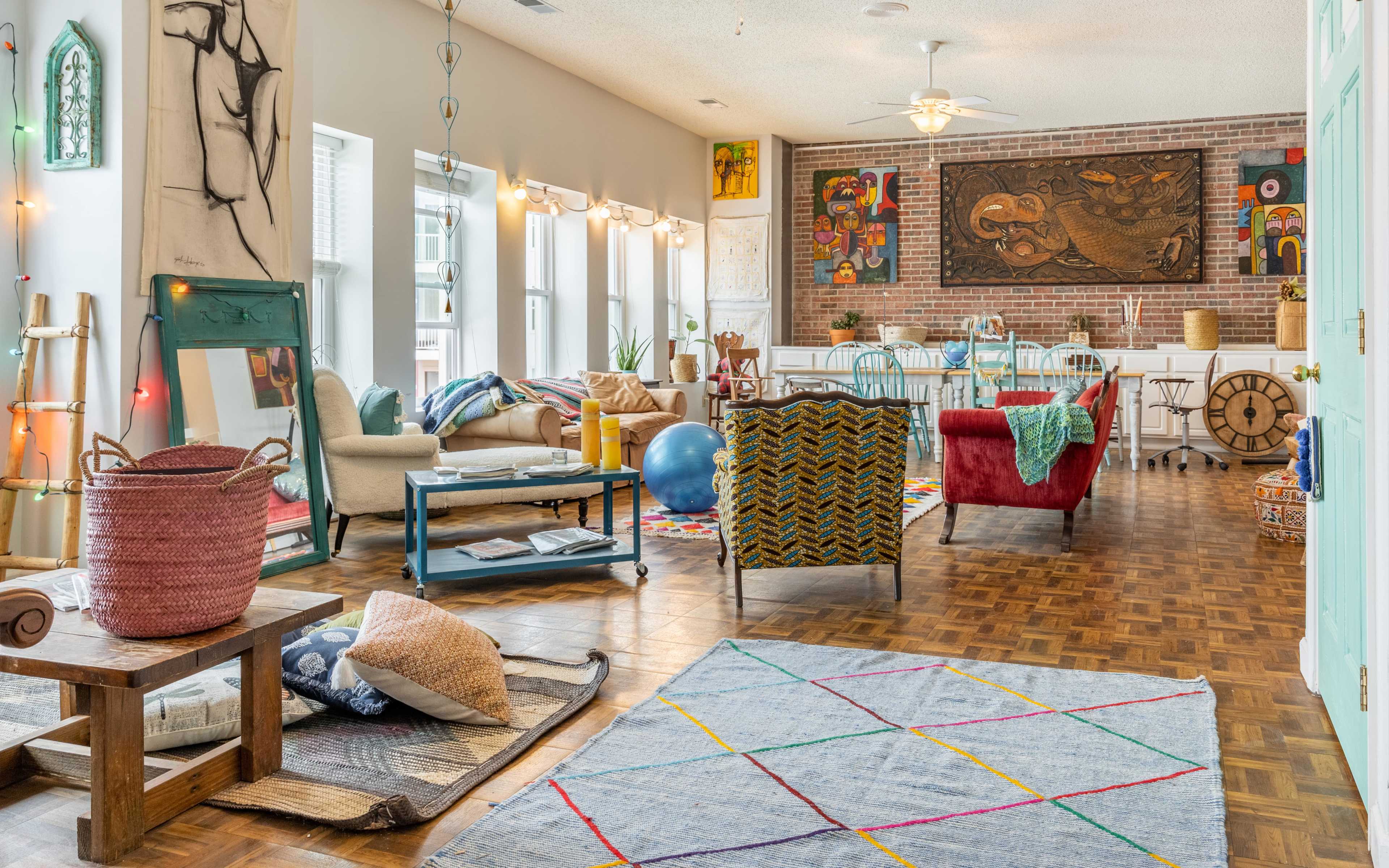 A bright, spacious living area with various seating options, colorful decor, and large windows allowing natural light in.