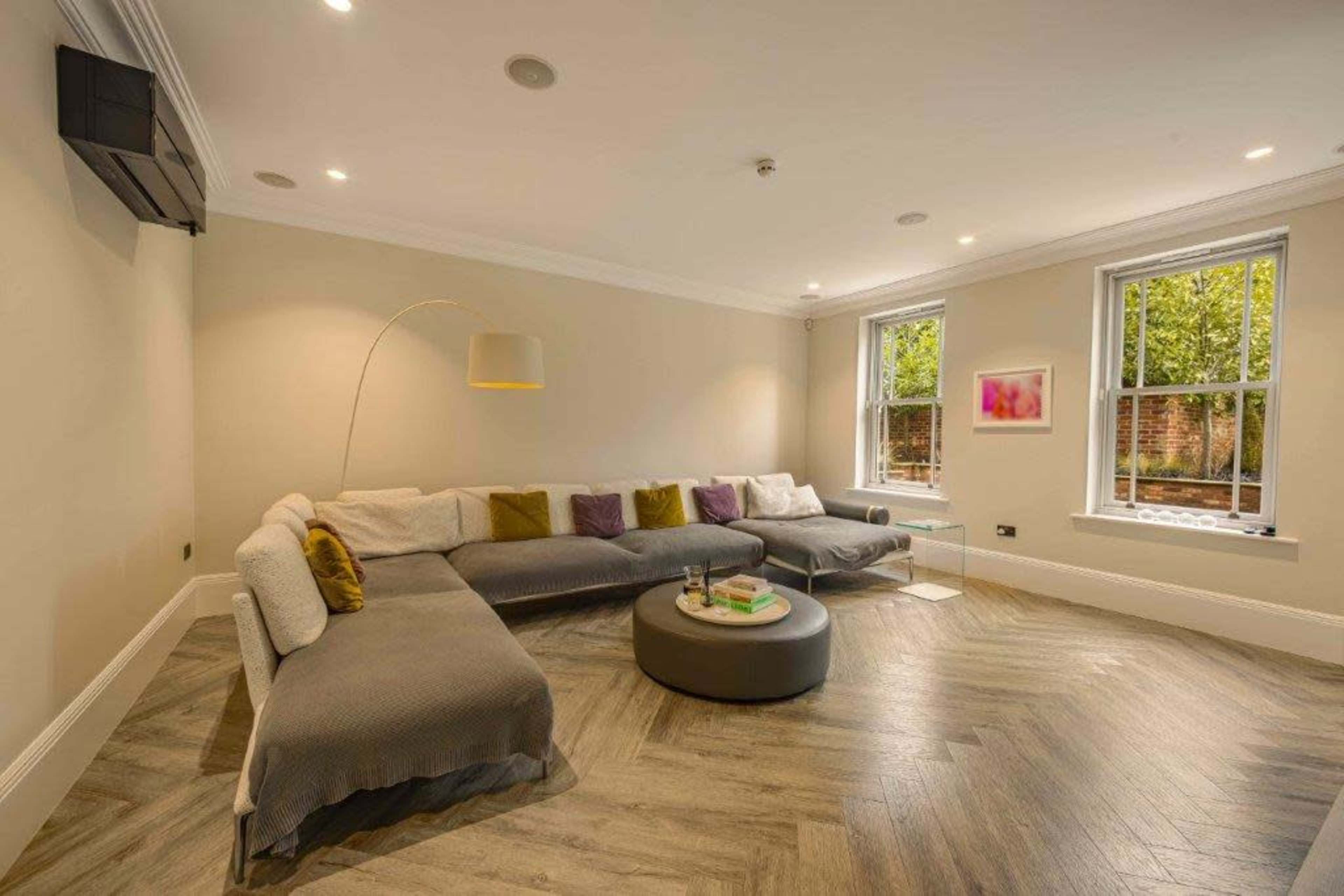 The image shows a modern living room with a large sectional sofa, a round coffee table, and windows that allow natural light to enter the space.