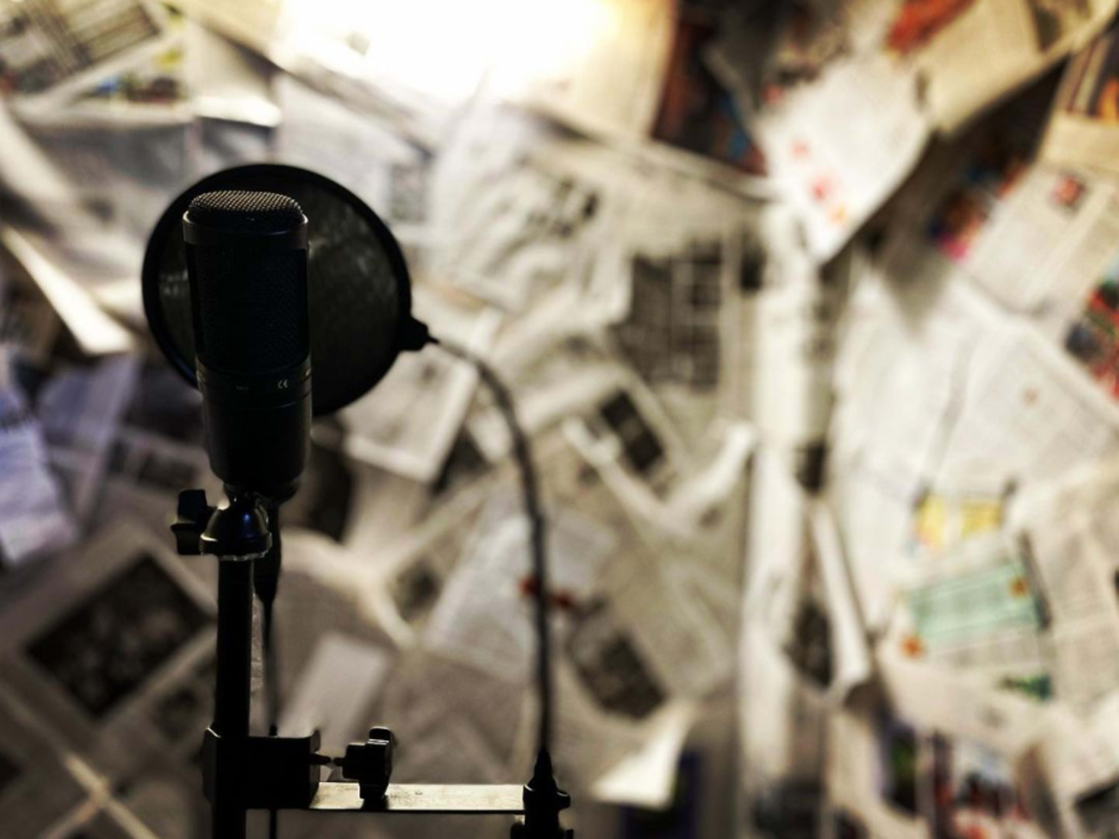 A microphone stands in front of a wall covered with newspapers.