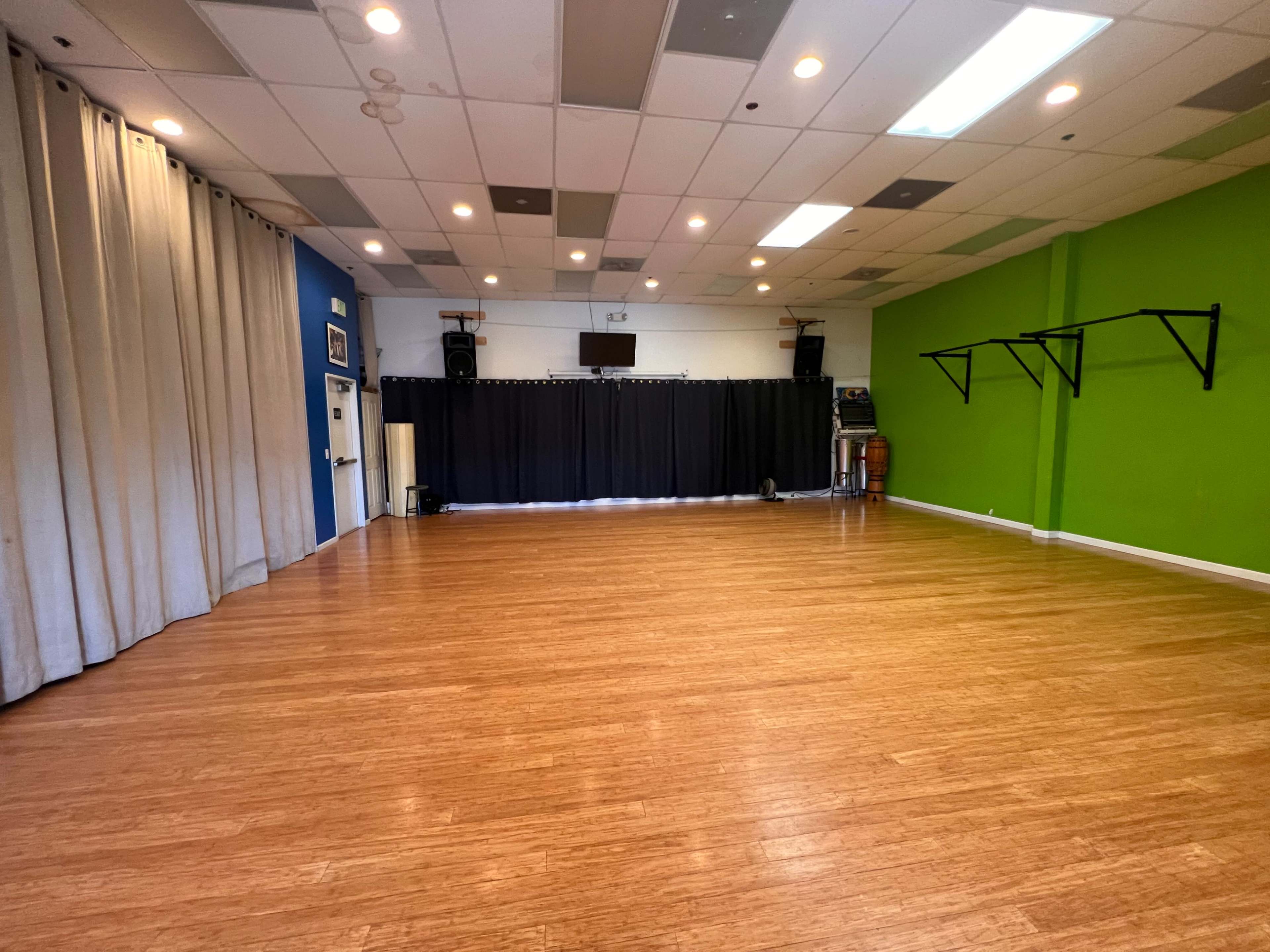 A spacious room with wooden flooring, blue and green walls, and a curtained area in the back.