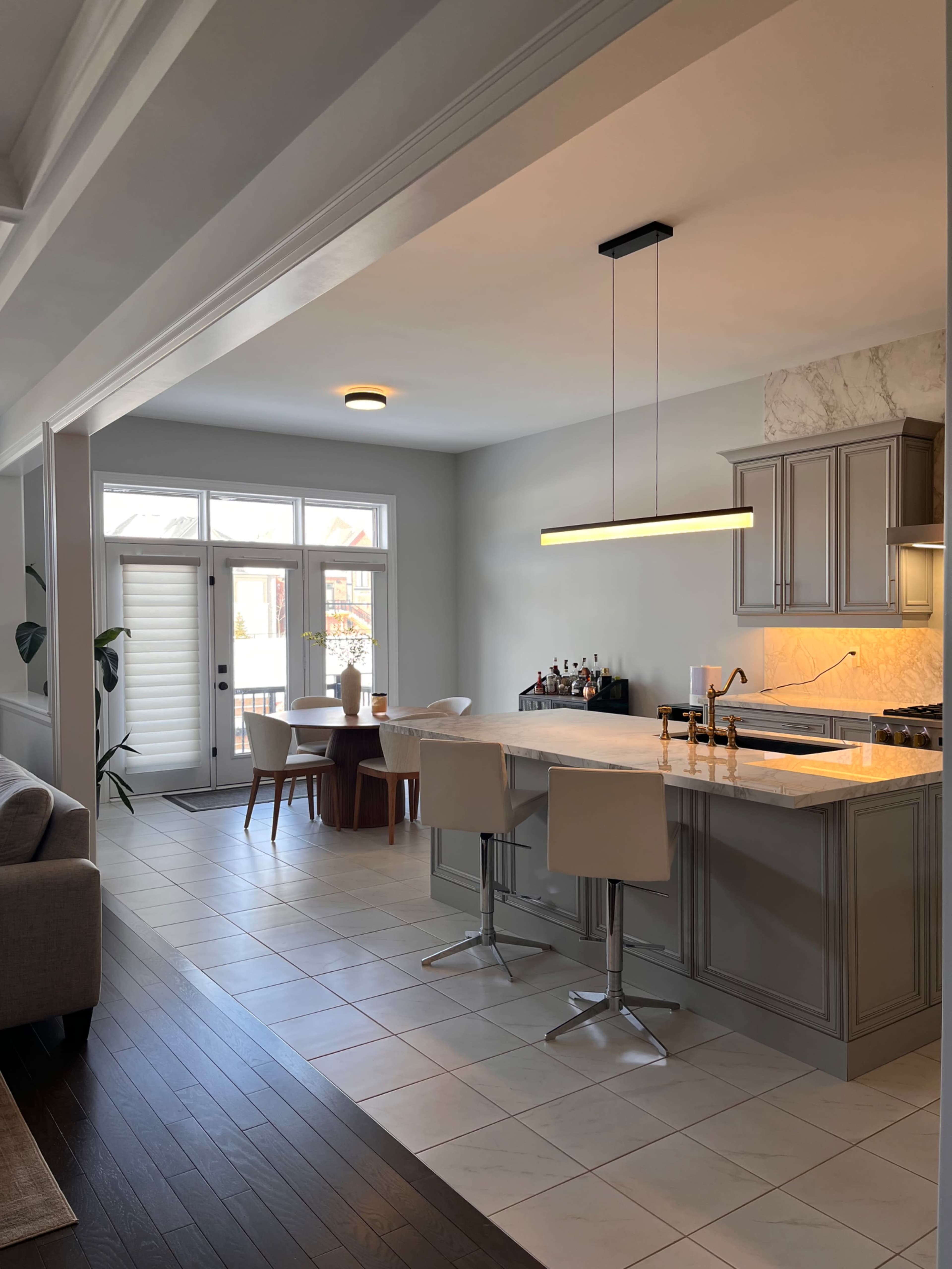 The image shows a modern kitchen open to a dining area, featuring a large island with bar stools, a dining table, and sliding glass doors leading to an outdoor space.
