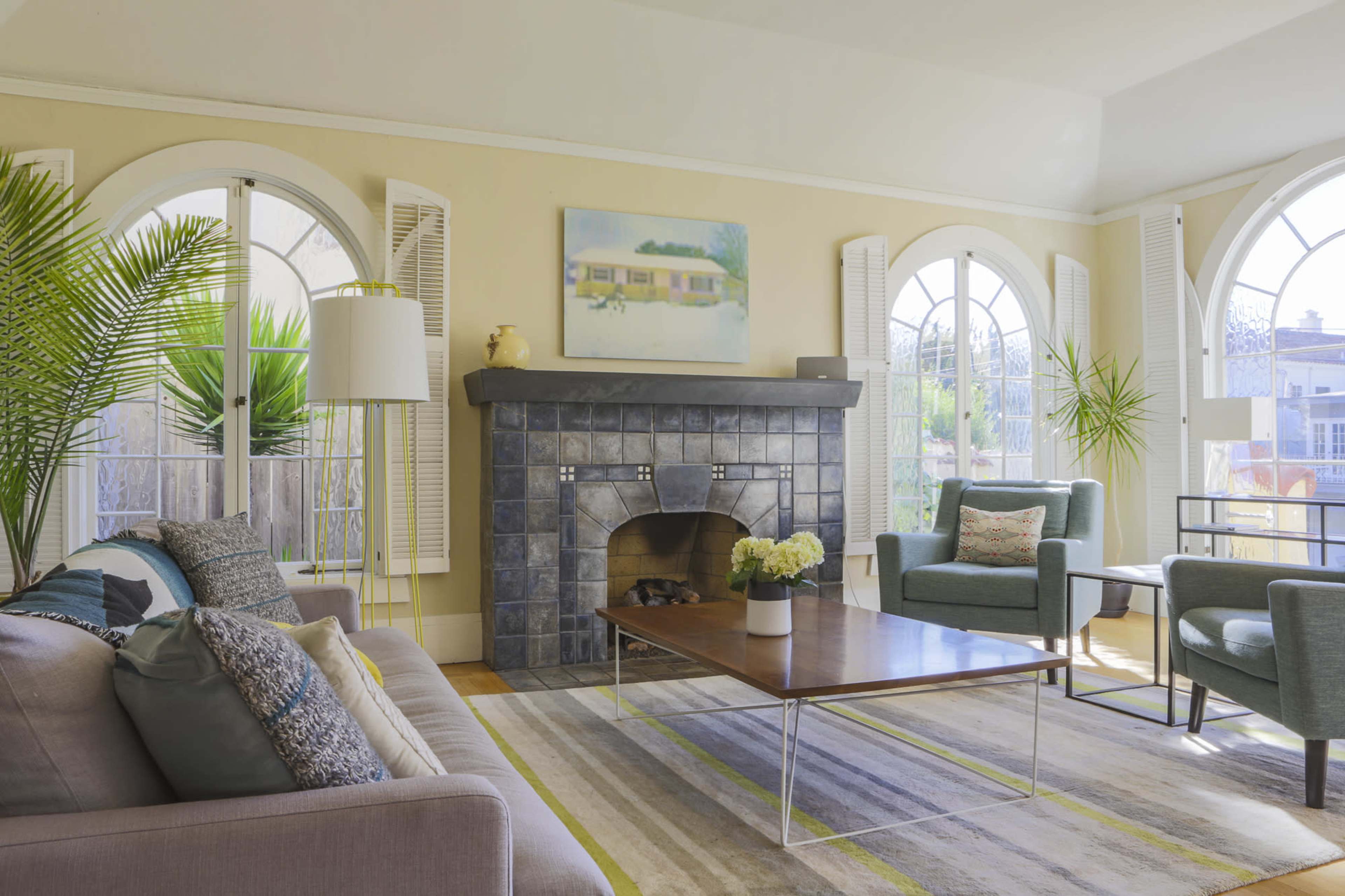 The living room features a tiled fireplace, modern furniture, and large arched windows allowing natural light in.