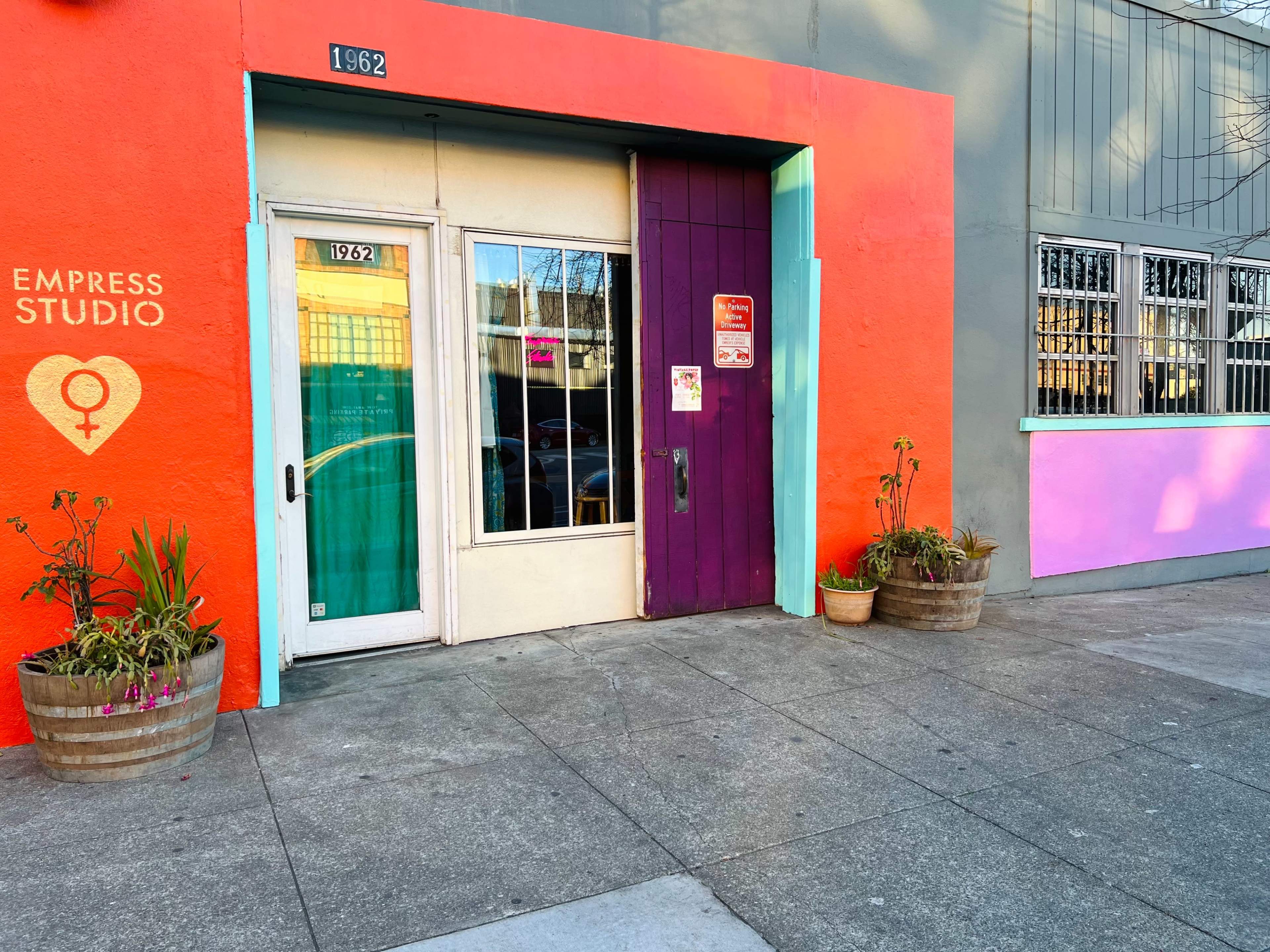 A brightly colored building facade with the text "Empress Studio" beside a purple door and planters on either side of the entrance.