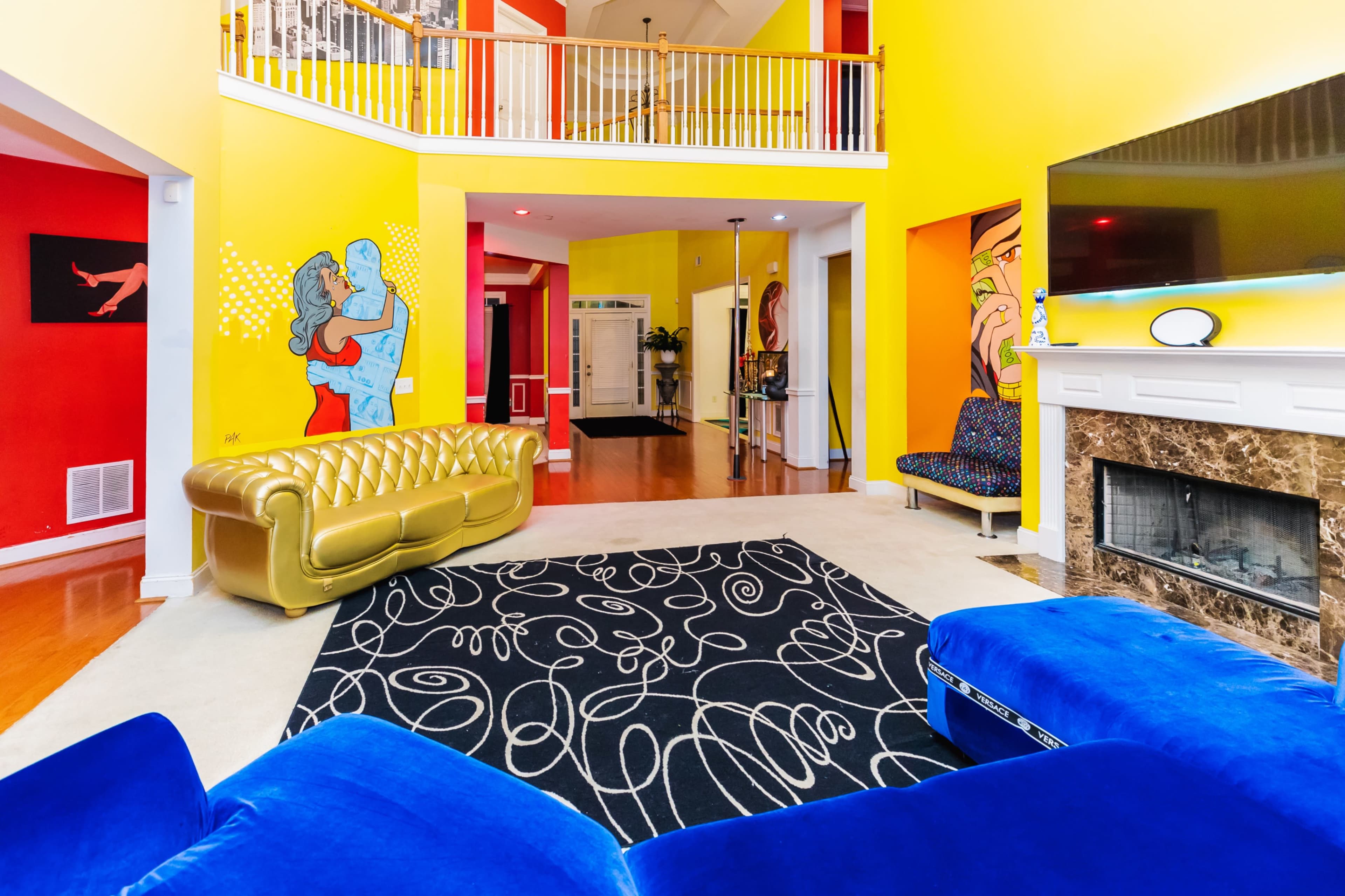 The living room features bold yellow walls, a gold sofa, a blue sectional, and a colorful mural alongside a fireplace.