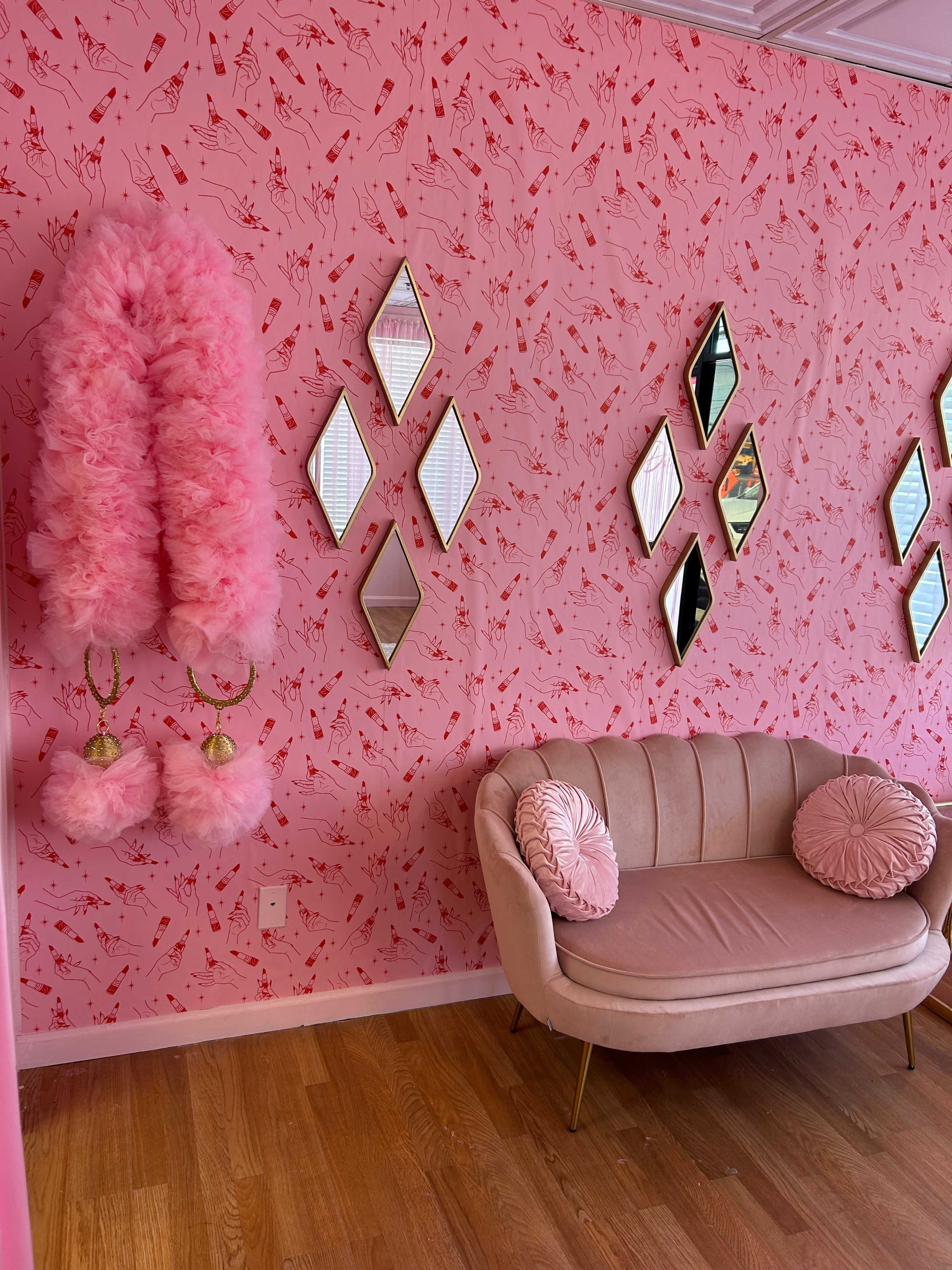 A pink-themed room with a patterned wall, a plush sofa, and decorative mirrors arranged in a diamond shape.