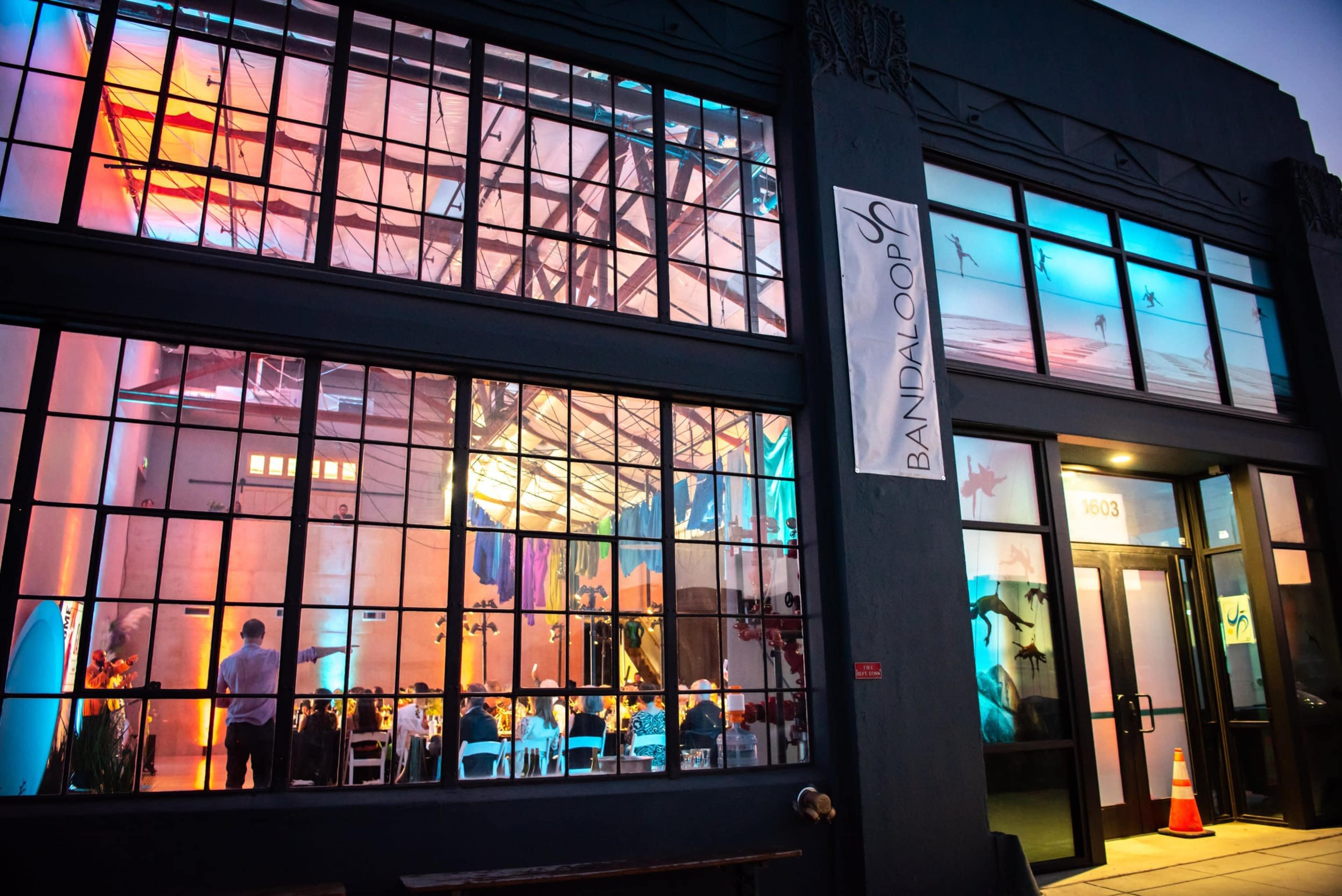 The image shows a large, well-lit event space through a glass window, with tables arranged for dining and colorful lighting creating an ambiance inside.