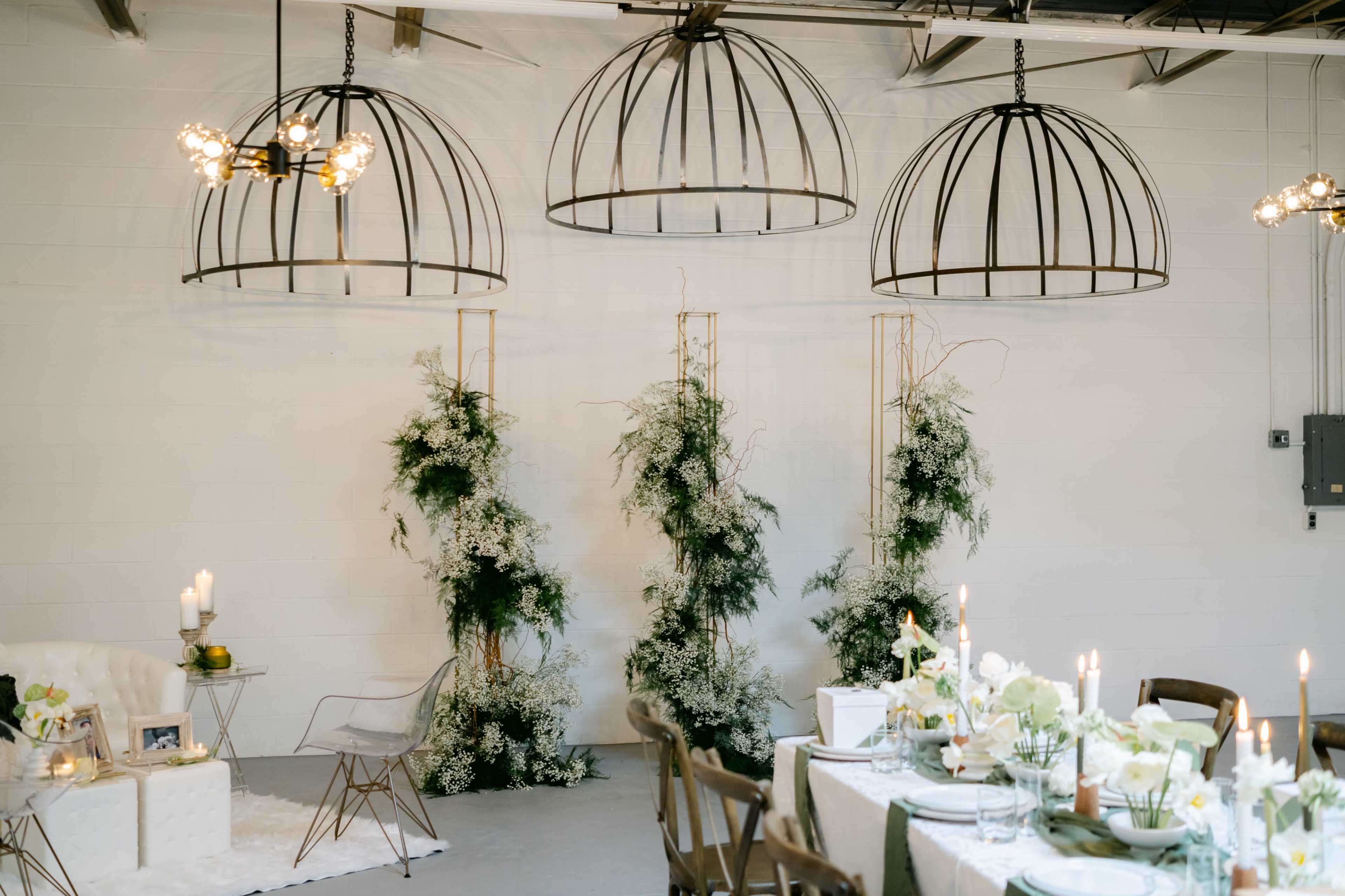 A spacious room featuring decorative hanging light fixtures, white walls, and elegantly arranged tables adorned with floral centerpieces.