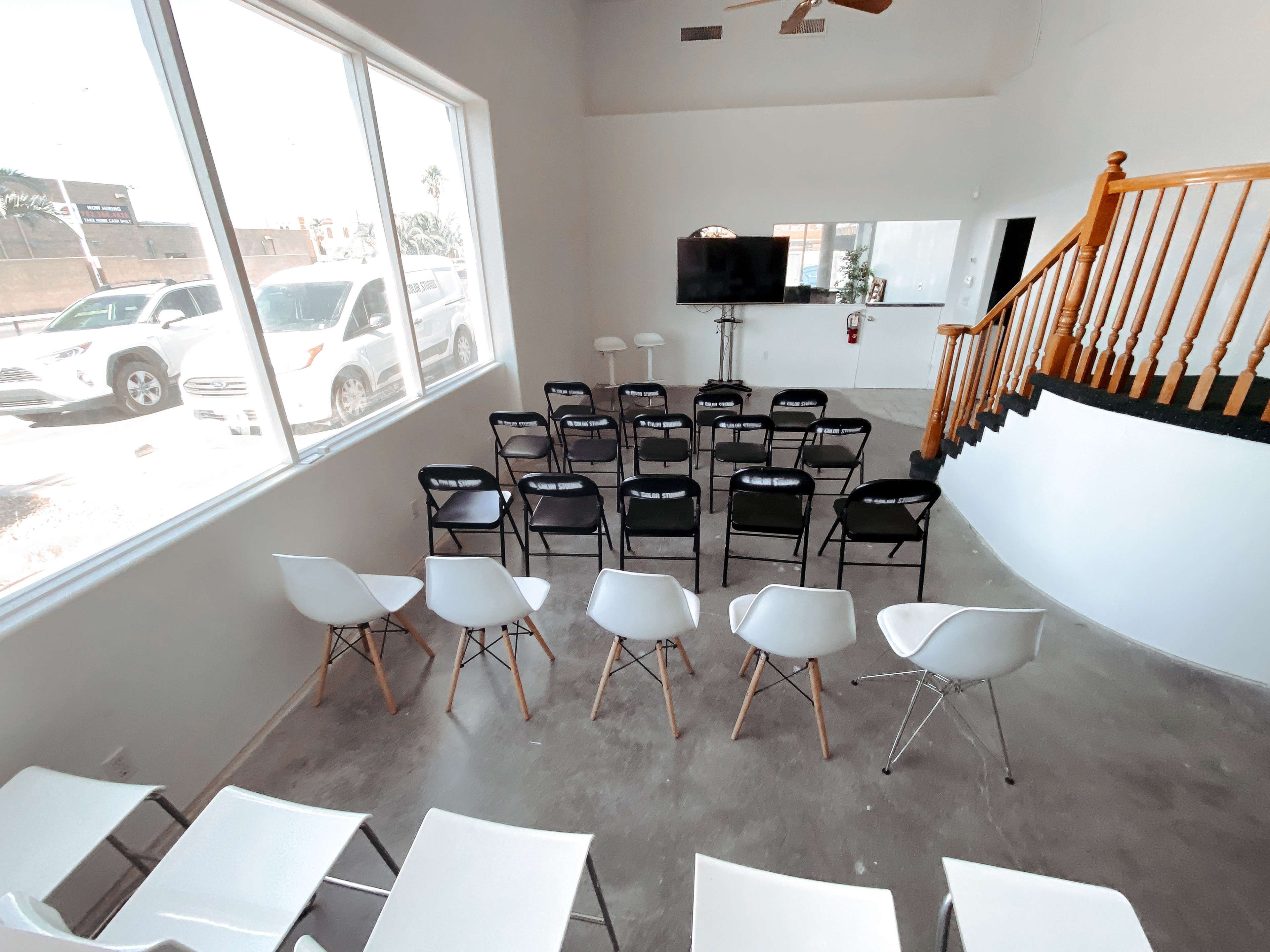 The room features a setup of rows of chairs facing a wall-mounted television, with large windows allowing natural light to enter.