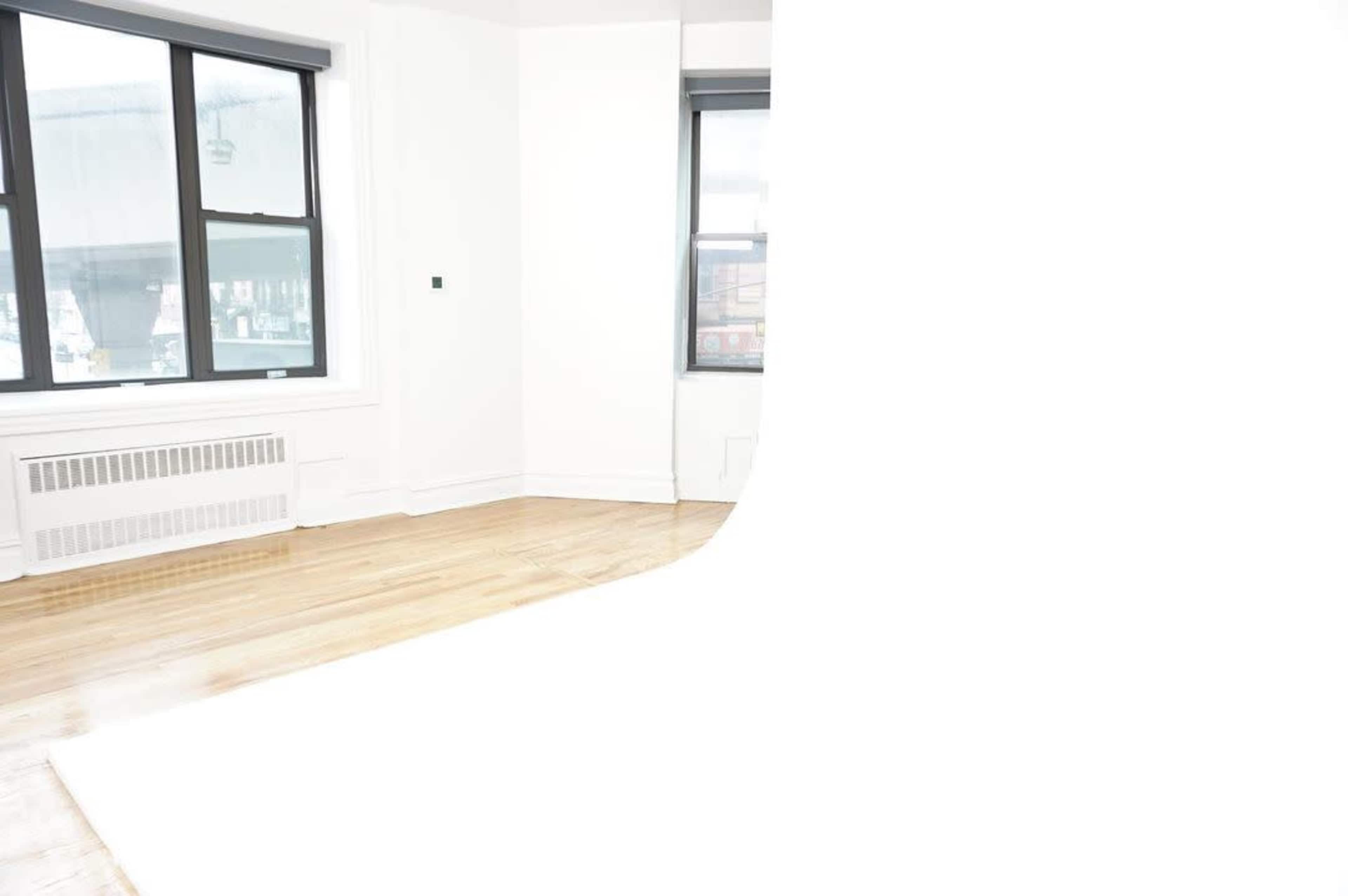 A bright, empty room with large windows, hardwood floors, and a smooth white backdrop extending from the floor to the ceiling.