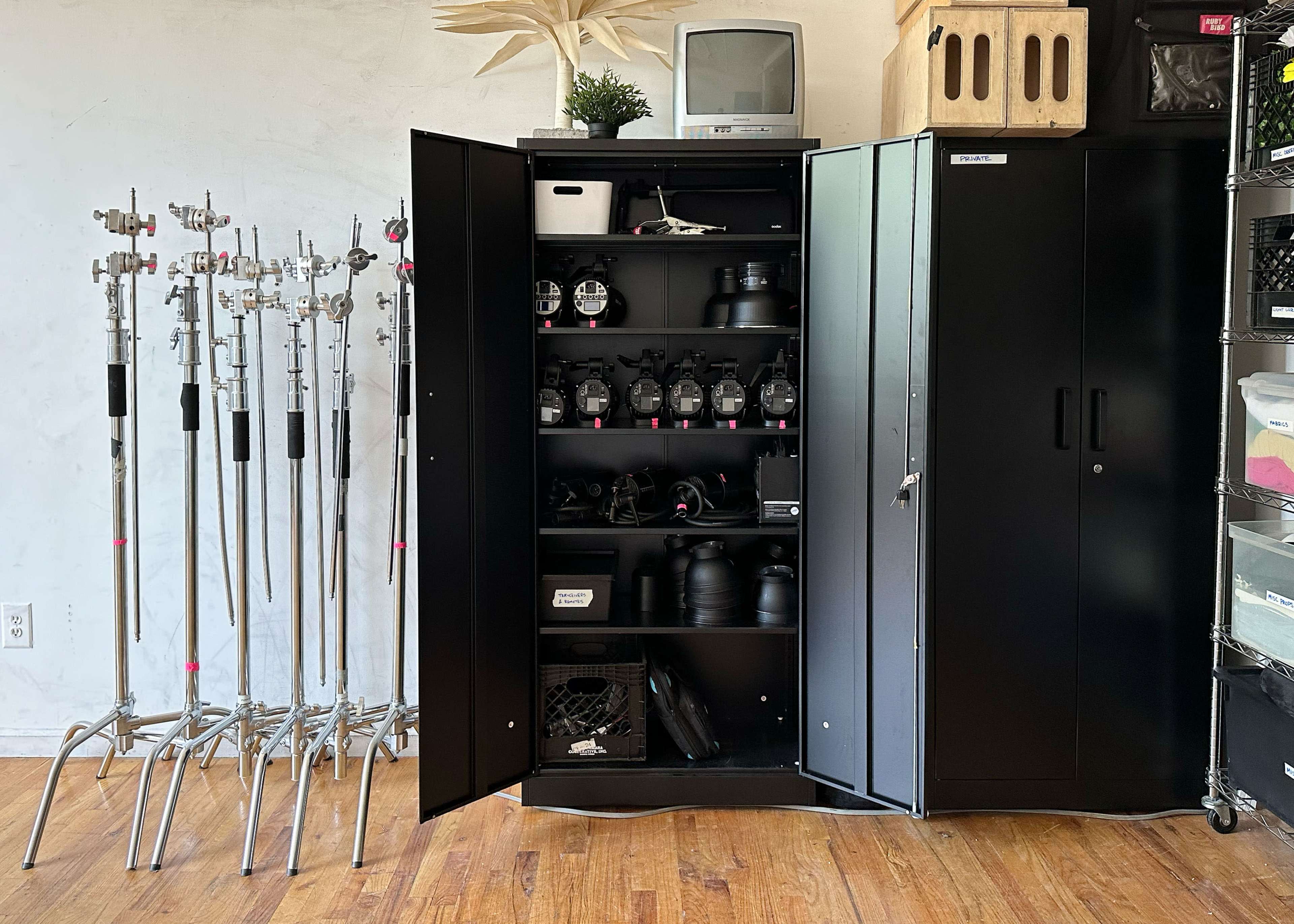 An open black storage cabinet filled with photography equipment, alongside several metal light stands.