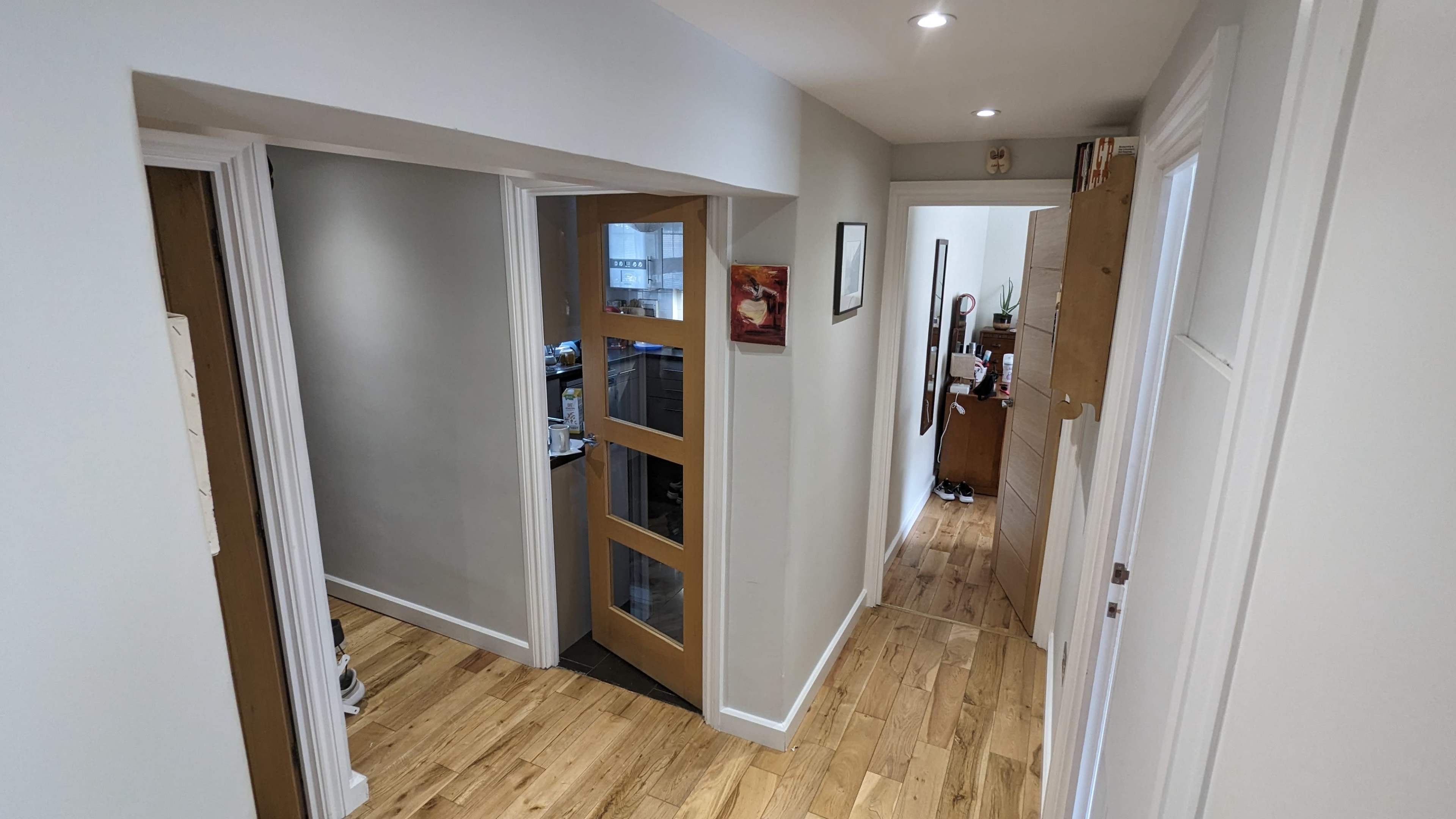 A hallway features two doorways and wooden flooring, with light-colored walls and recessed lighting.