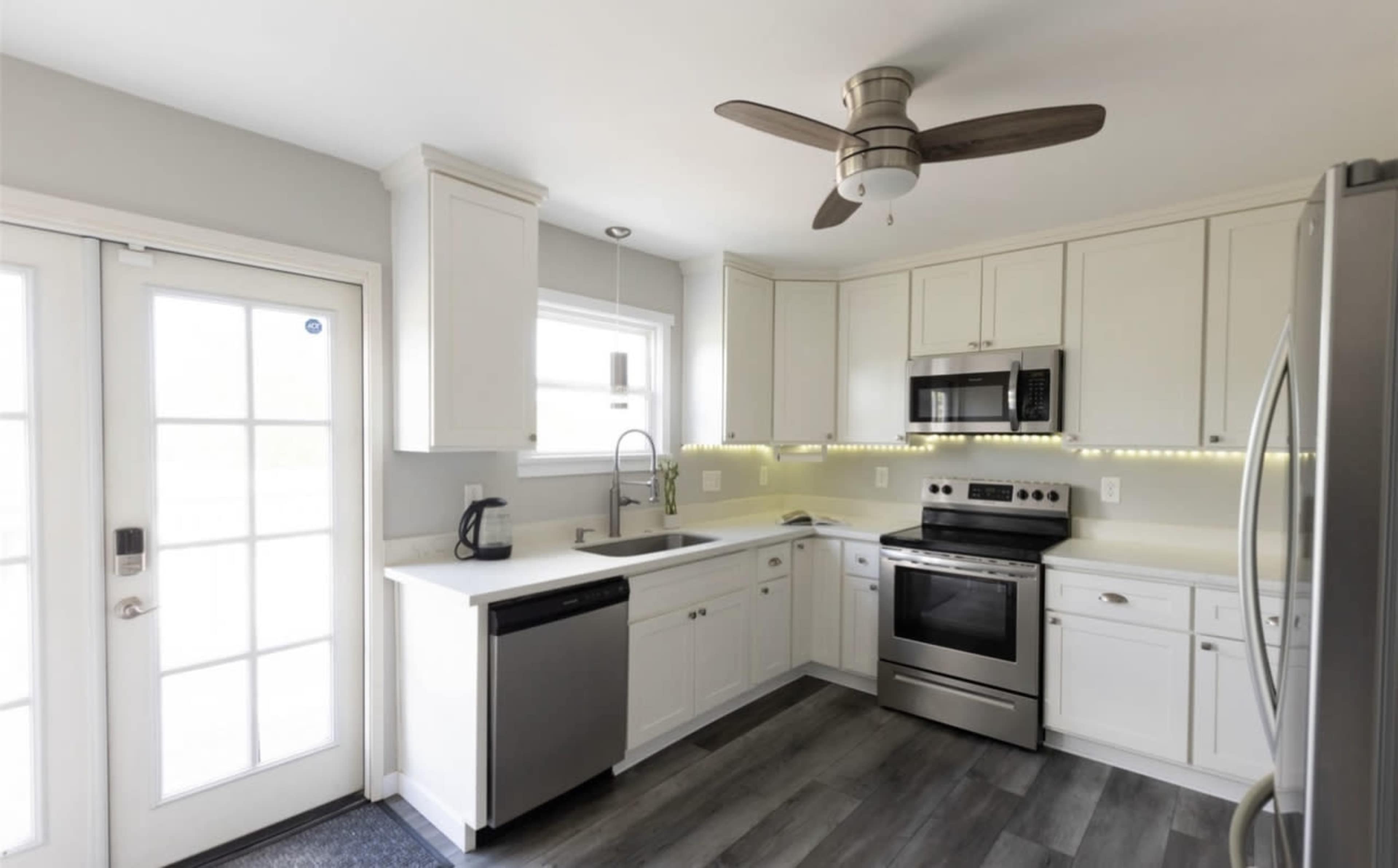 The image shows a modern kitchen with white cabinetry, stainless steel appliances, and a ceiling fan.