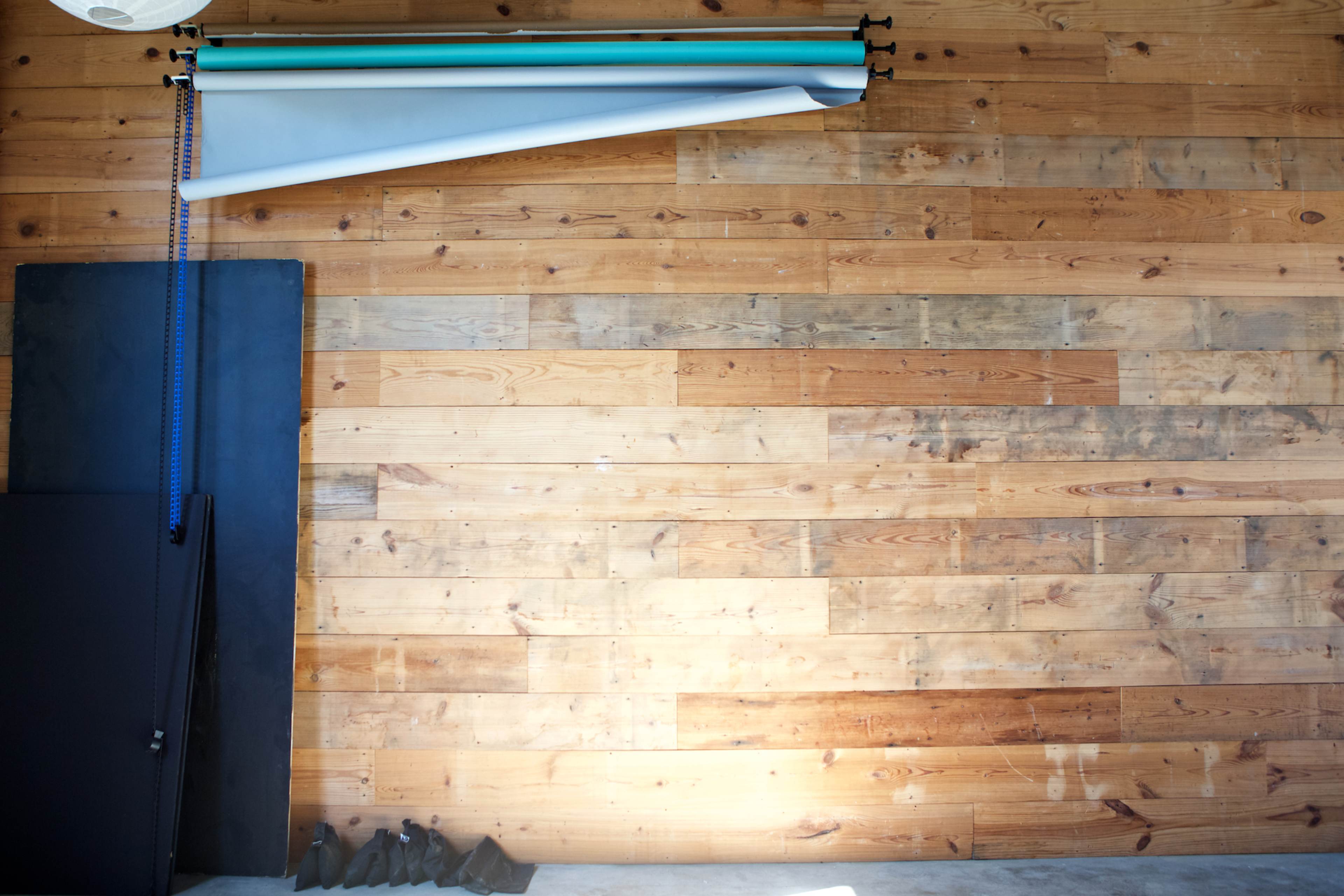The image shows a wall made of wooden planks with a paper roll mounted above it and several dark-colored objects on the floor.