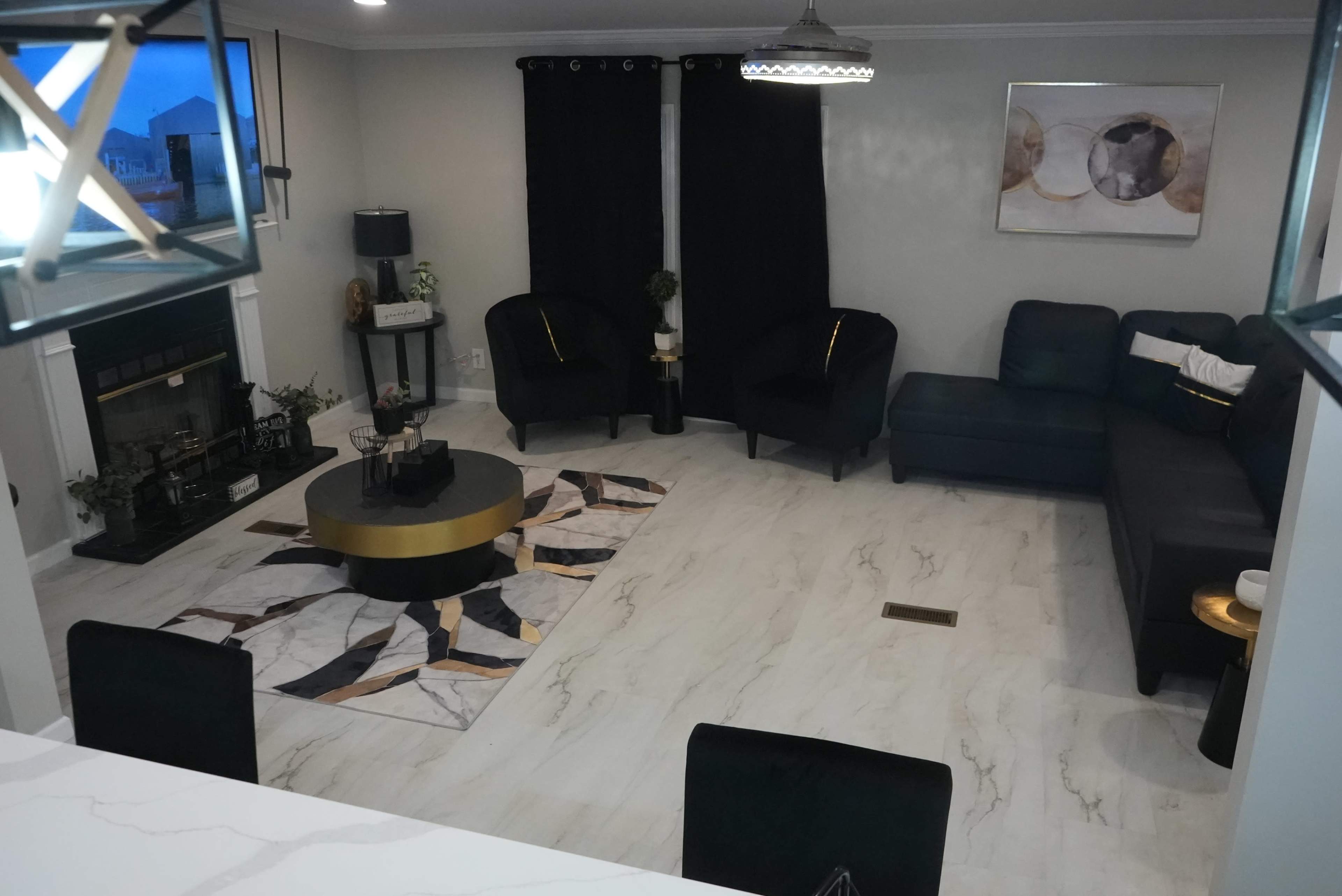 The image shows a modern living room with a large sectional sofa, two black chairs, a circular coffee table, and a patterned rug on a light-colored floor.