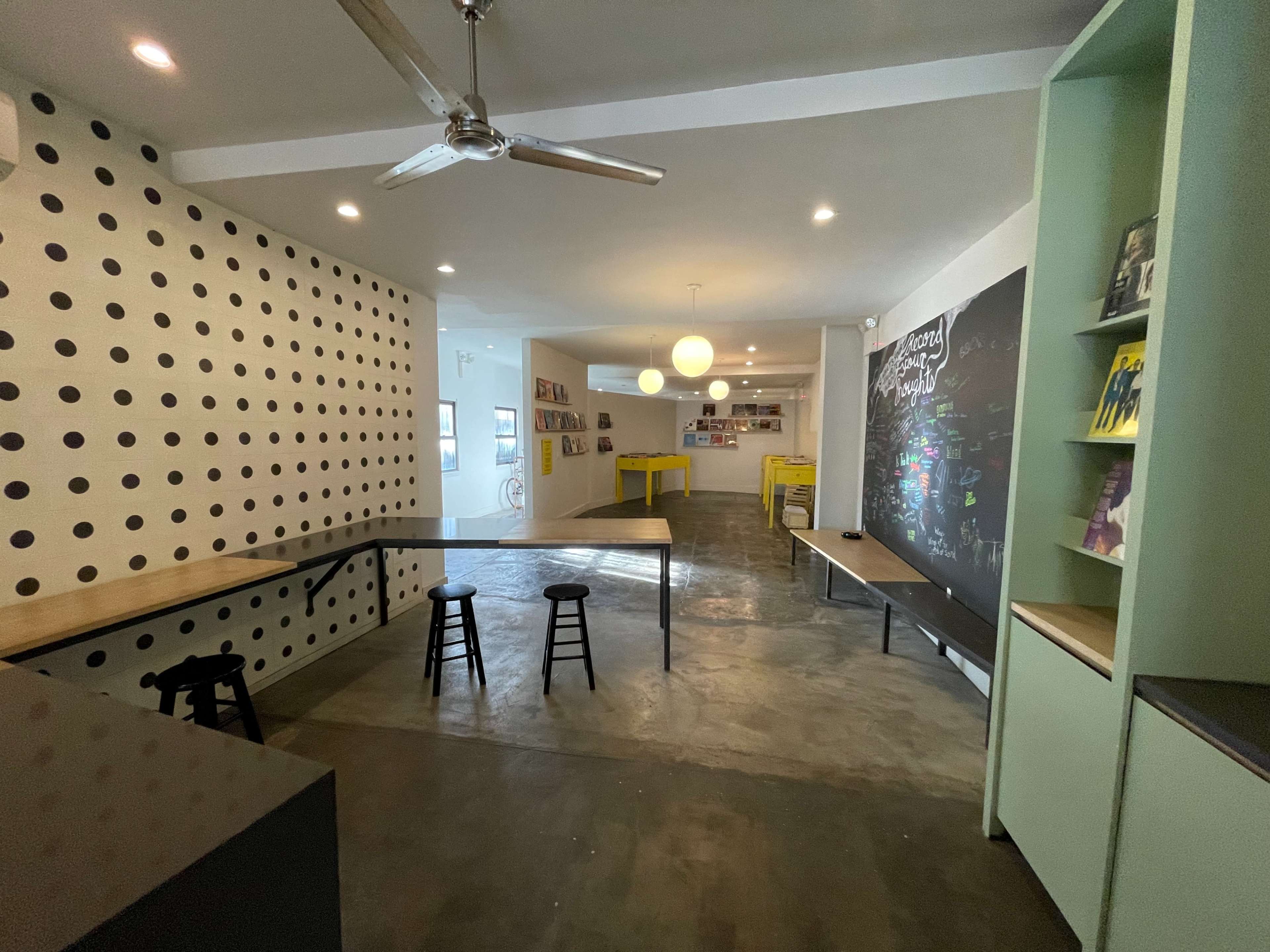 A modern, open space with two tables, high stools, a polka-dotted wall, and a chalkboard on one side.