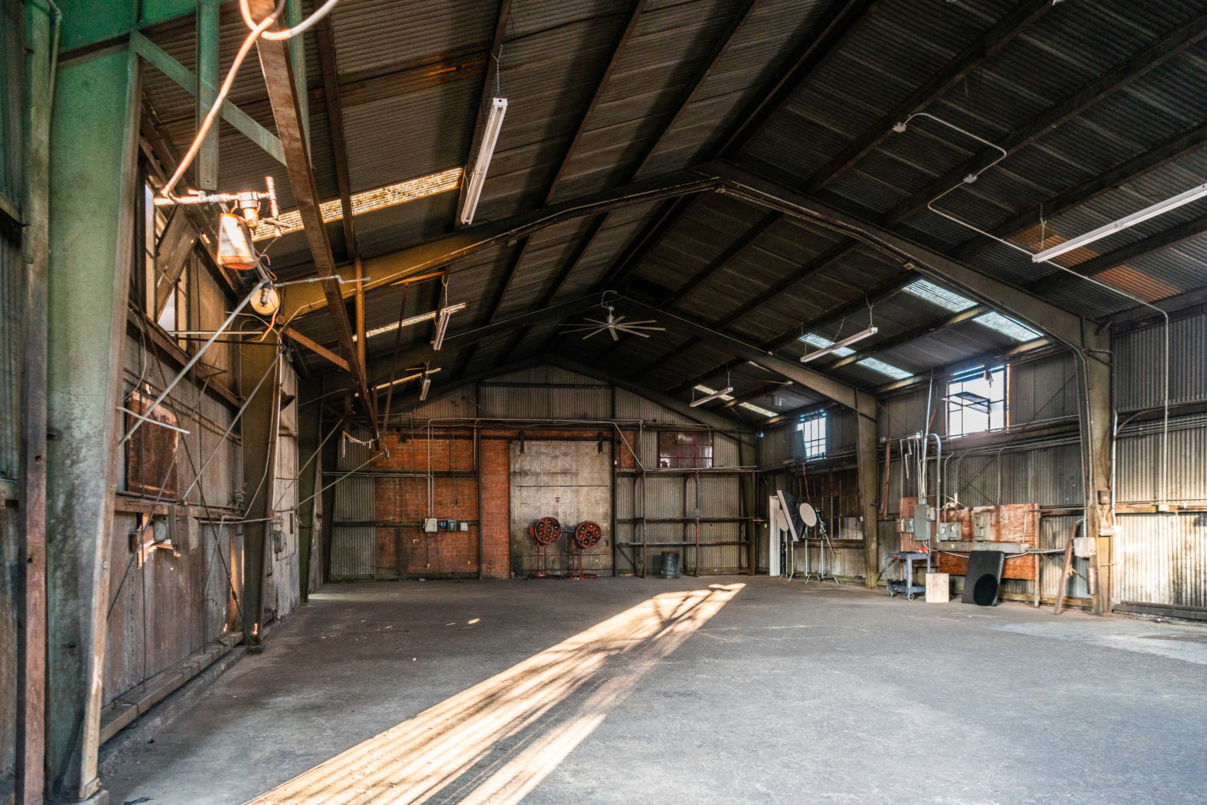 The interior of a spacious industrial warehouse with high ceilings, exposed beams, and minimal furnishings.