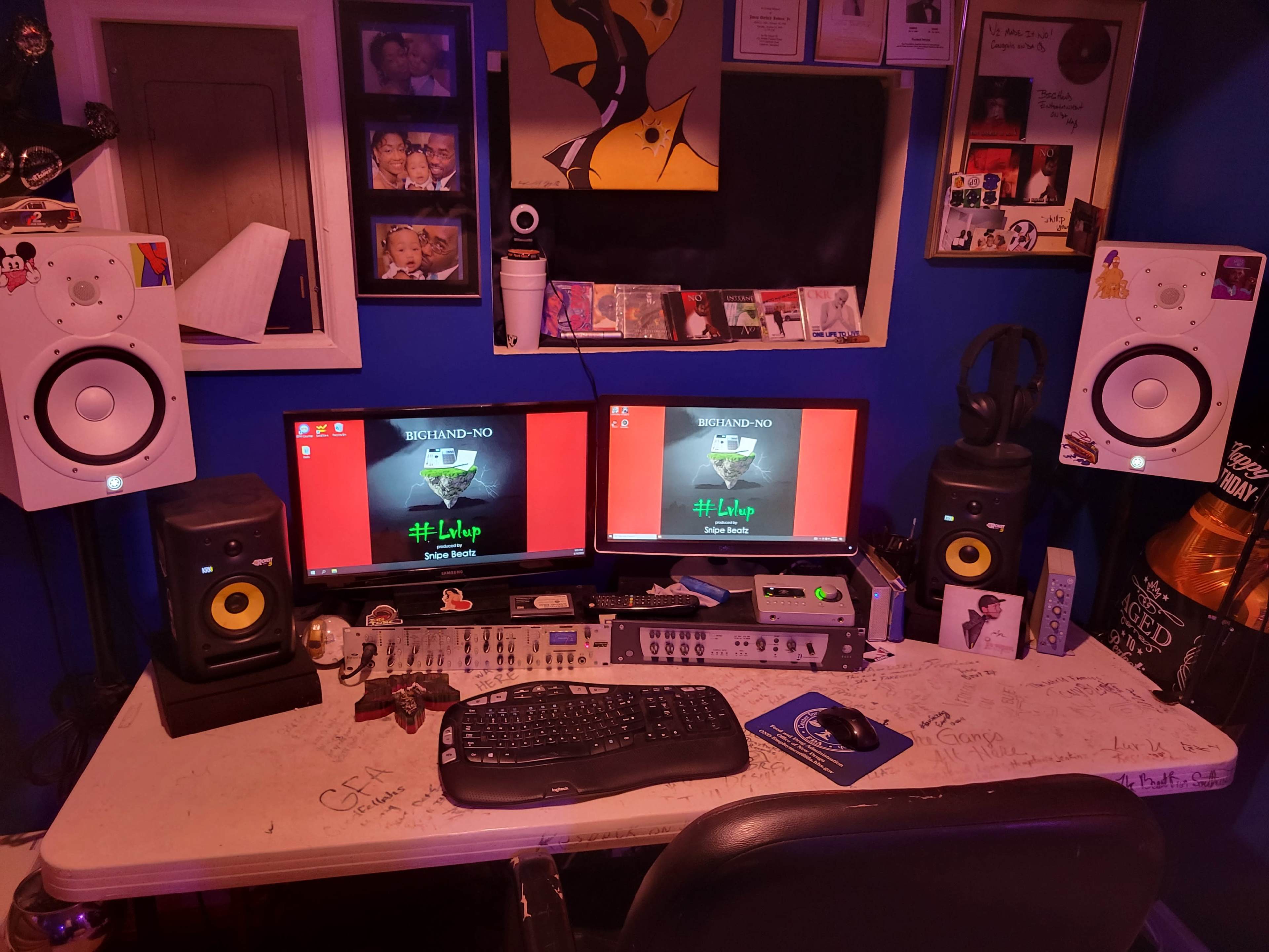 A workstation with two computer monitors, studio speakers, a keyboard, and audio equipment in a blue-walled room filled with various decorations and personal items.