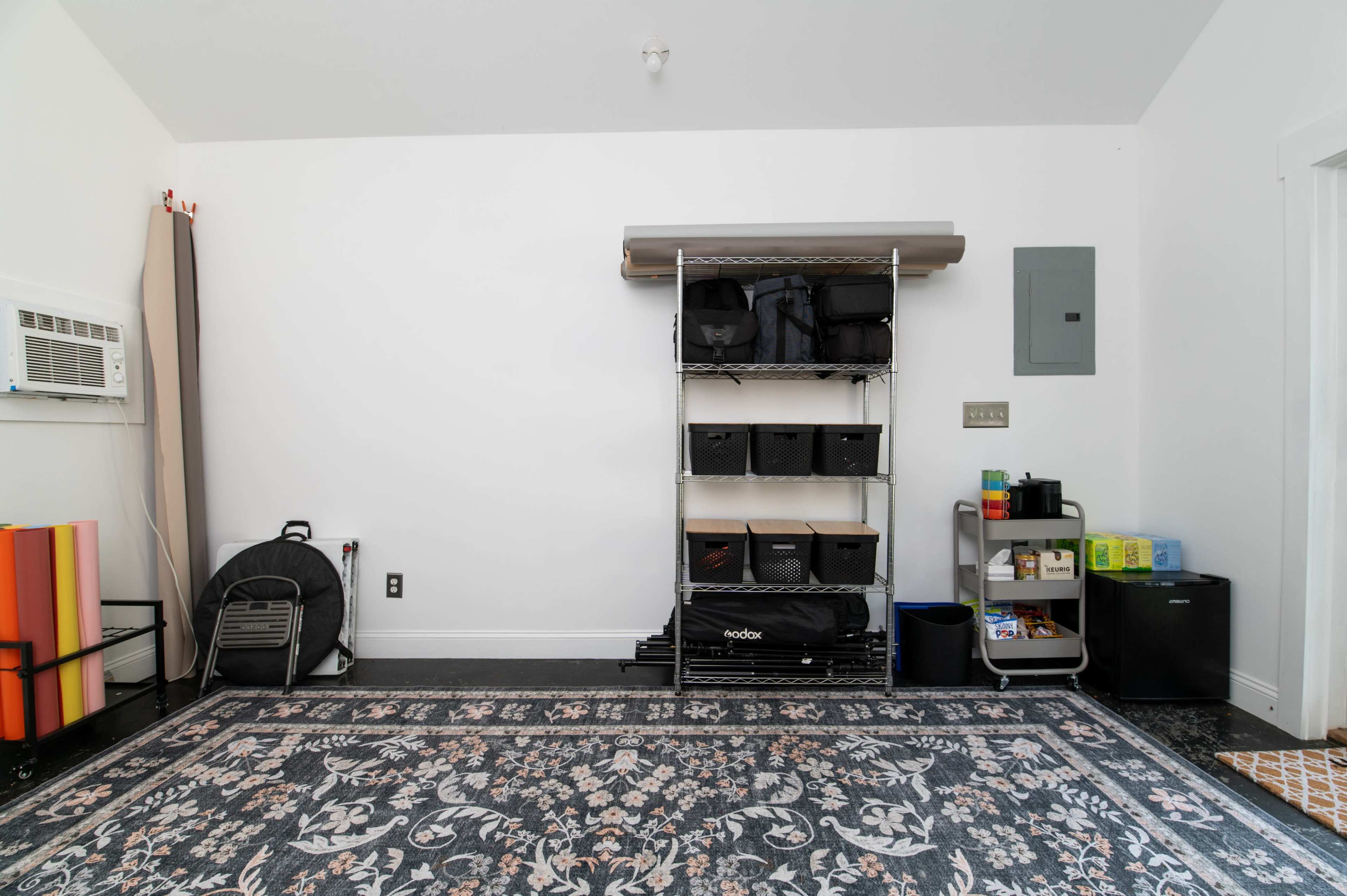 The image shows a clean garage or storage room with a shelf holding bins, an air conditioning unit, and minimal decorative elements on the floor.