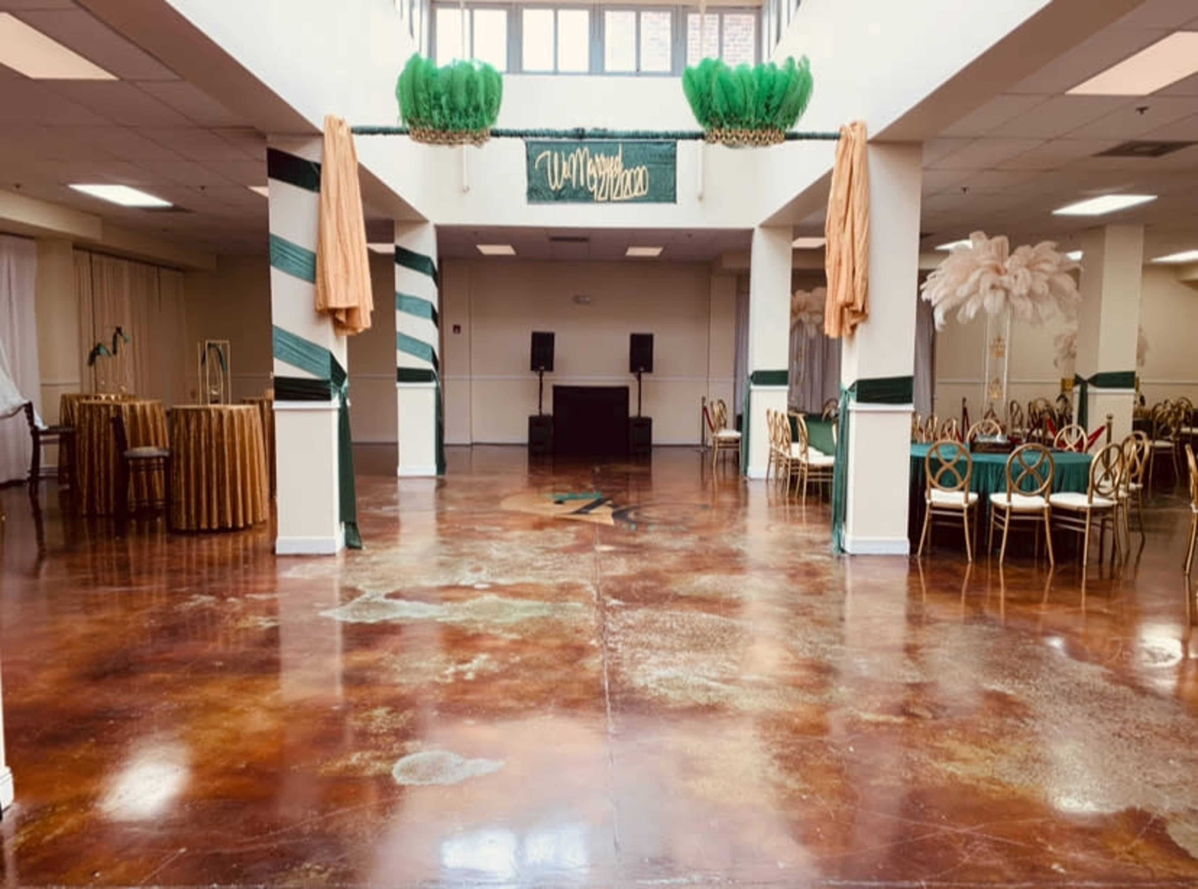 The image shows an empty event space featuring polished concrete floors, decorated columns, and several tables and chairs arranged for an event.