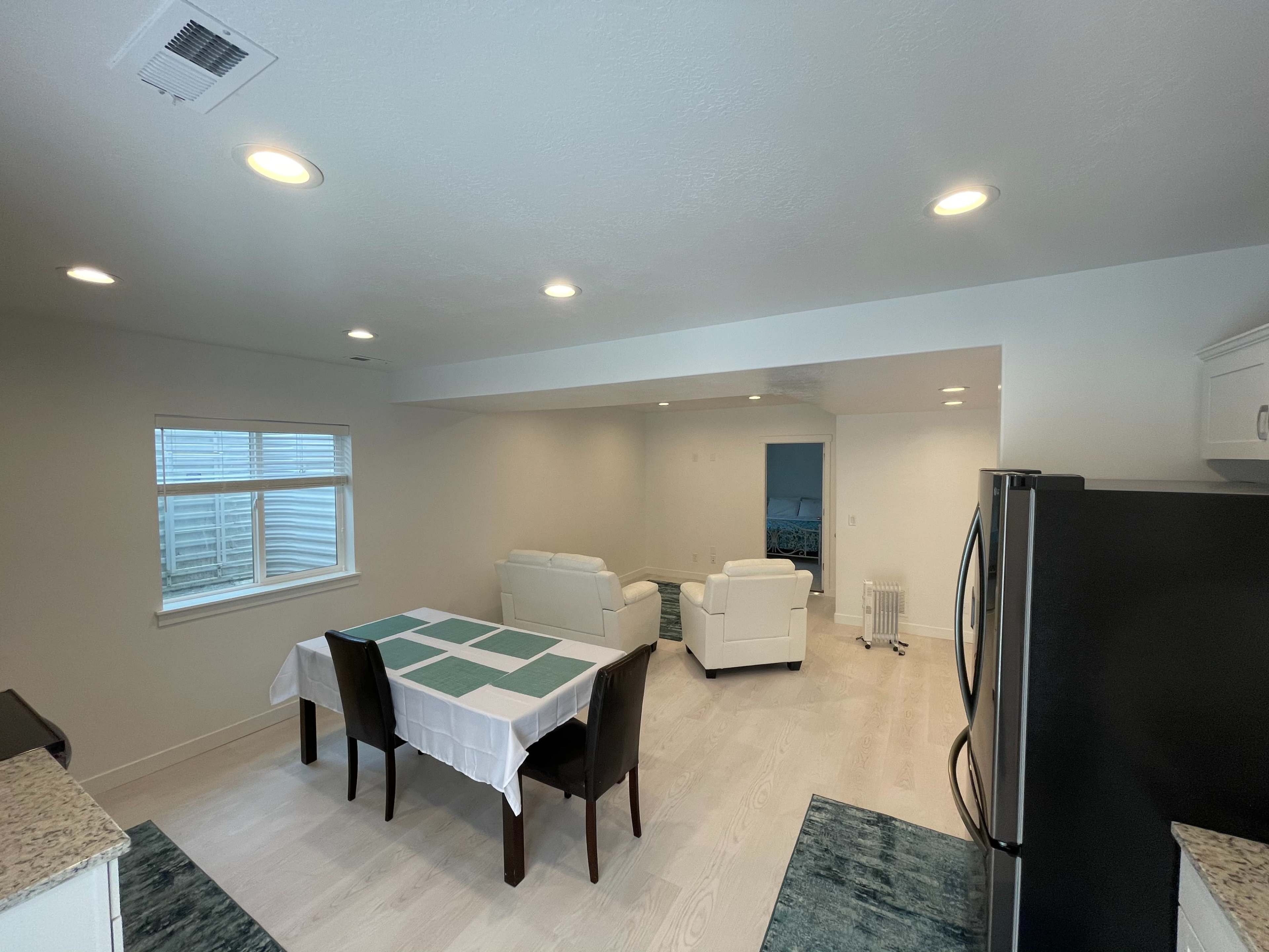 A modern kitchen and dining area featuring a table with a white tablecloth, four chairs, and two sofas in a well-lit, open-layout space.