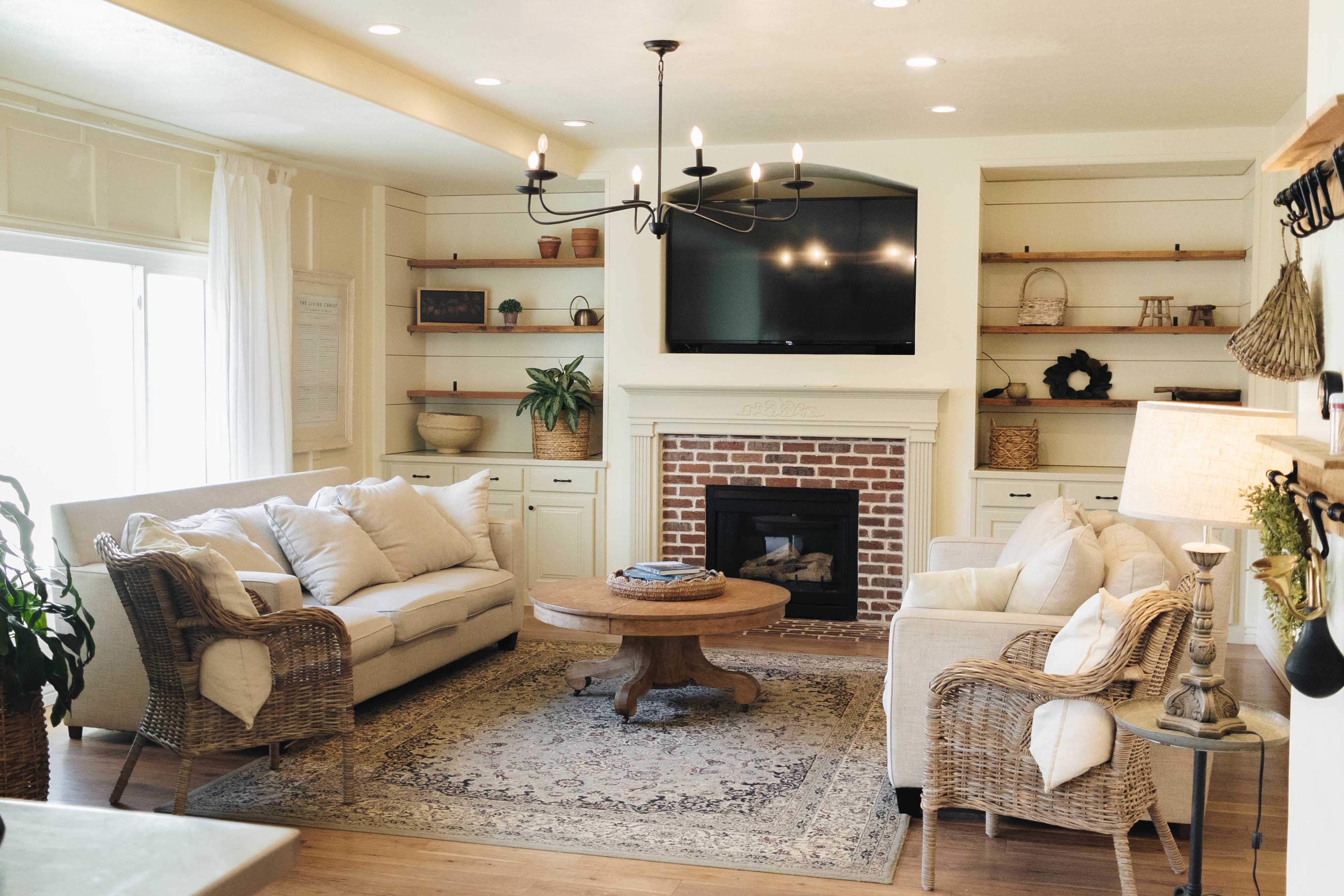 The living room features two sofas, a round wooden coffee table, and a fireplace with built-in shelving, all under a chandelier.