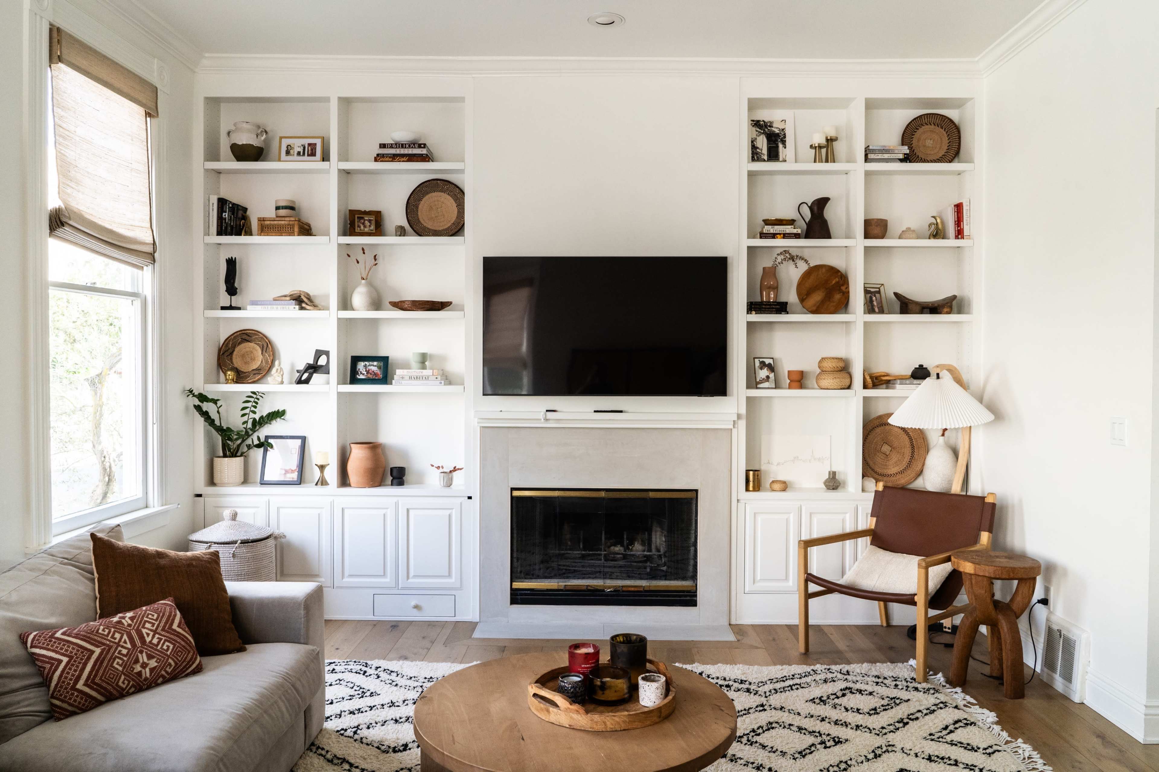 A living room features built-in shelves filled with decorative items, a television mounted above a fireplace, and a coffee table in front of a beige sofa.