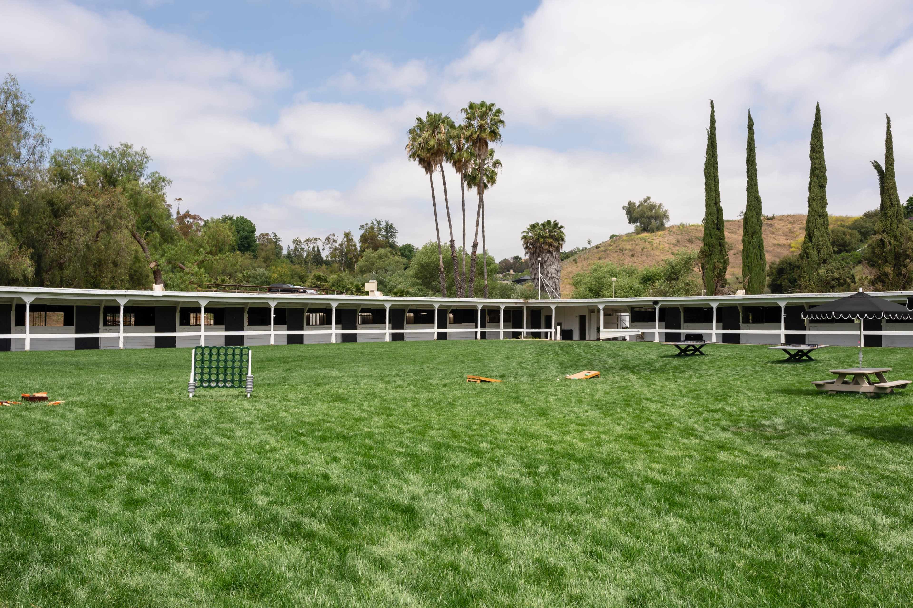 A spacious green lawn surrounded by low, white buildings and palm trees under a partly cloudy sky.