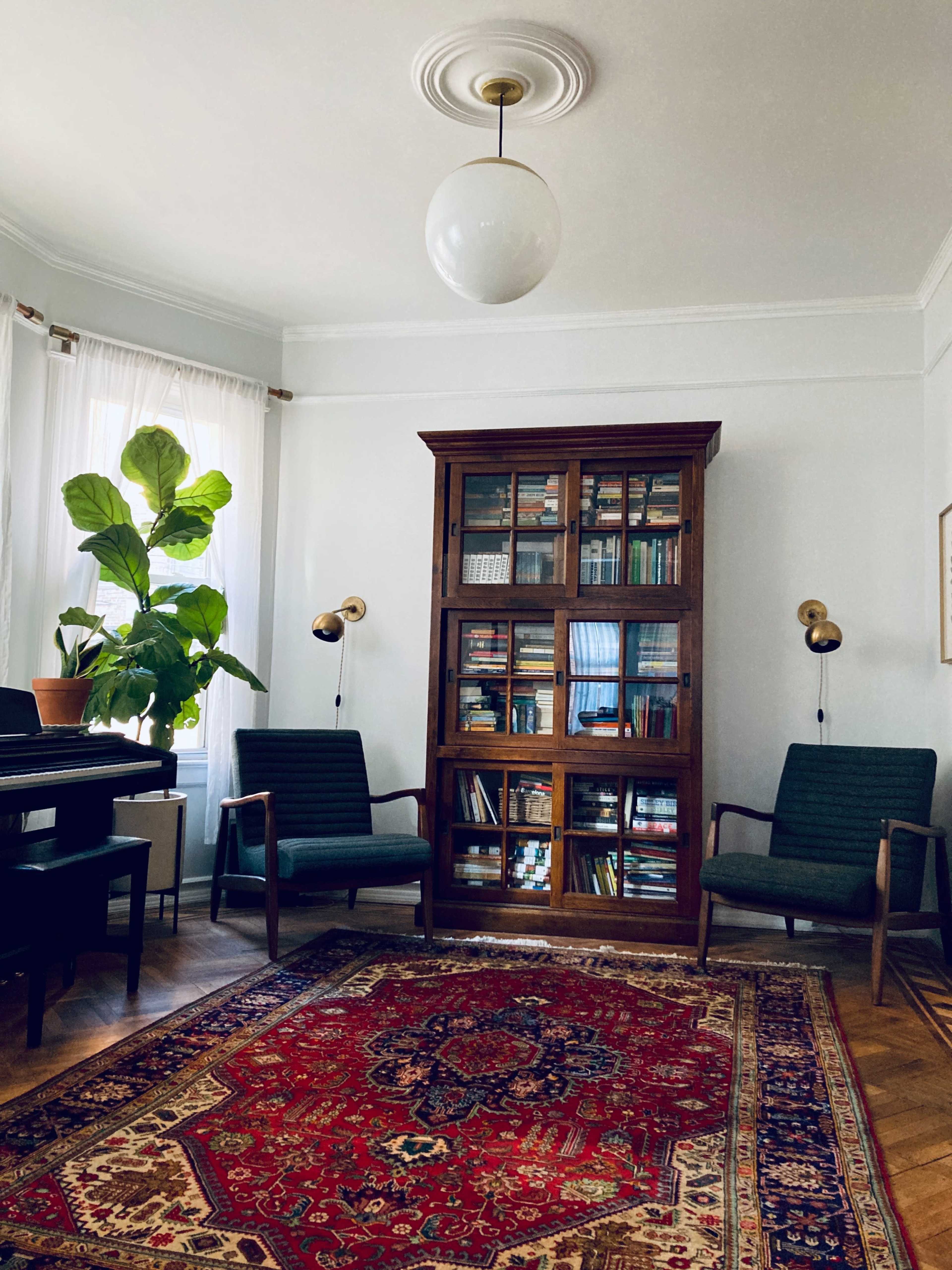 A living room with a wooden bookshelf, two green chairs, a potted plant, and a decorative rug.