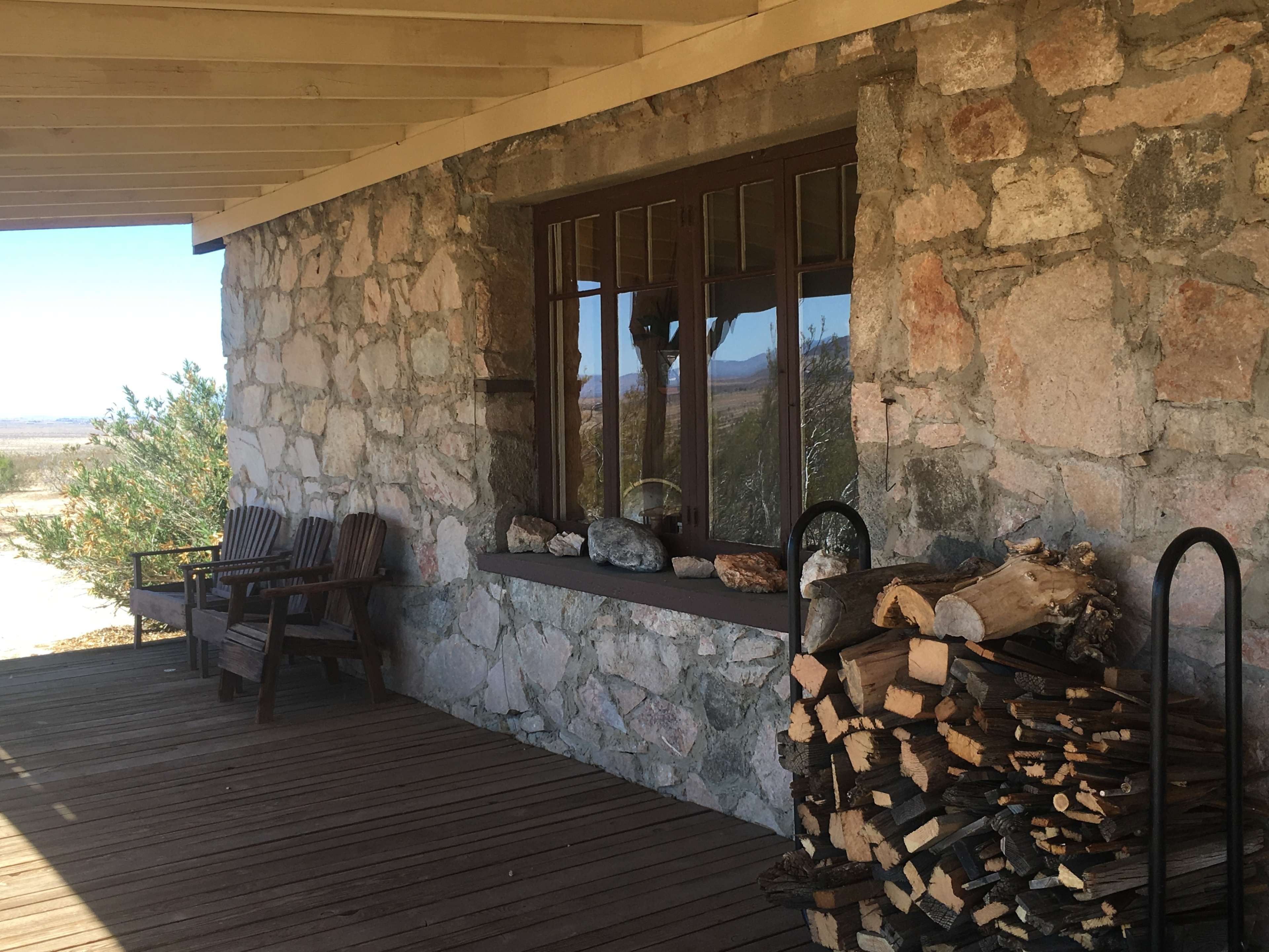 The image shows a stone building's porch with a stack of firewood and wooden seating.
