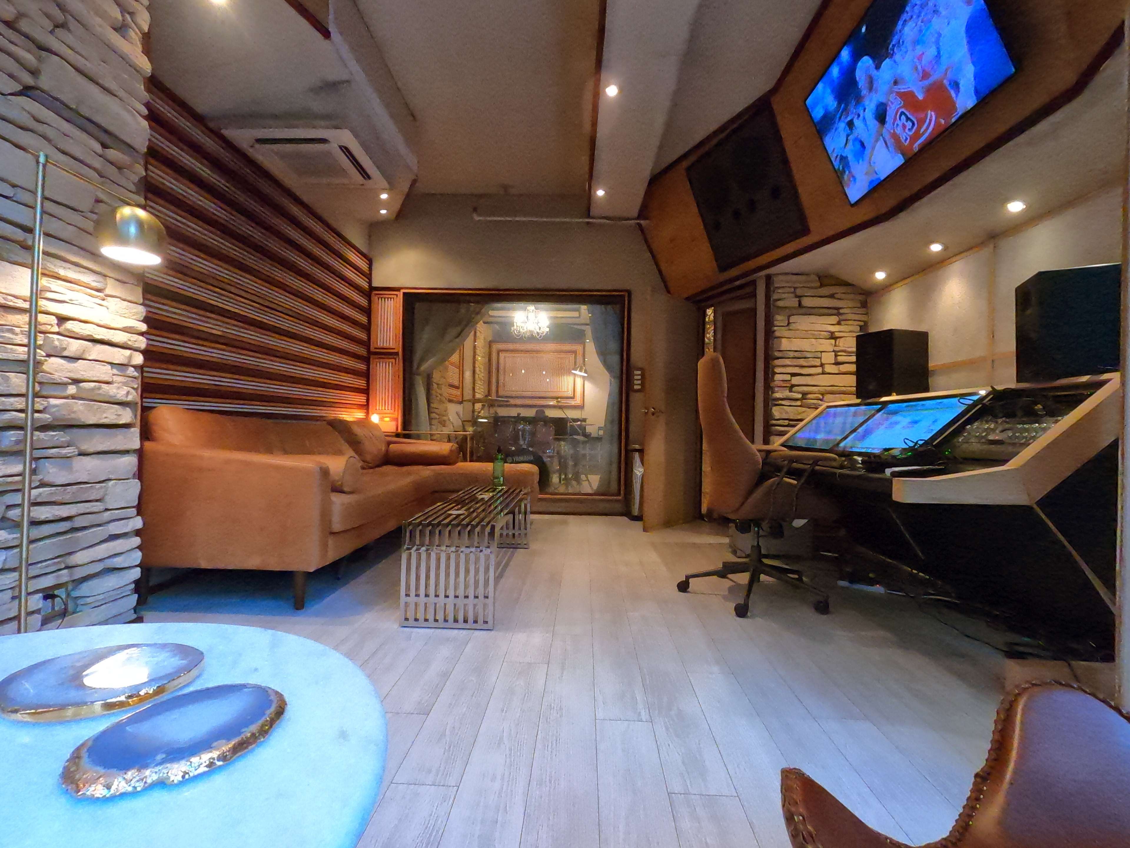 A modern studio space featuring a lounge area with a sofa and a coffee table, alongside a sound mixing console and large screens.
