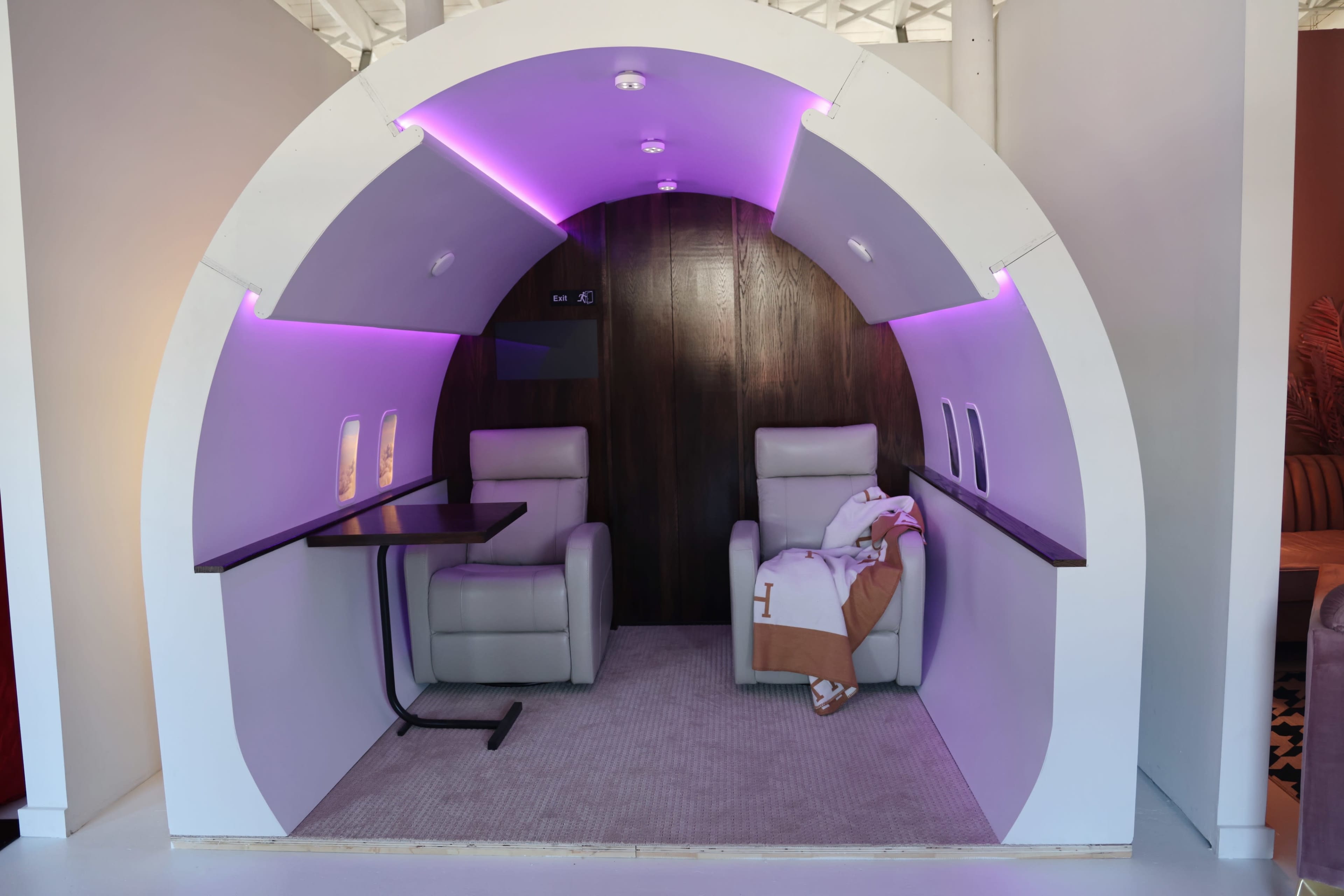A futuristic, curved seating area designed like an airplane cabin, featuring two armchairs and ambient lighting.