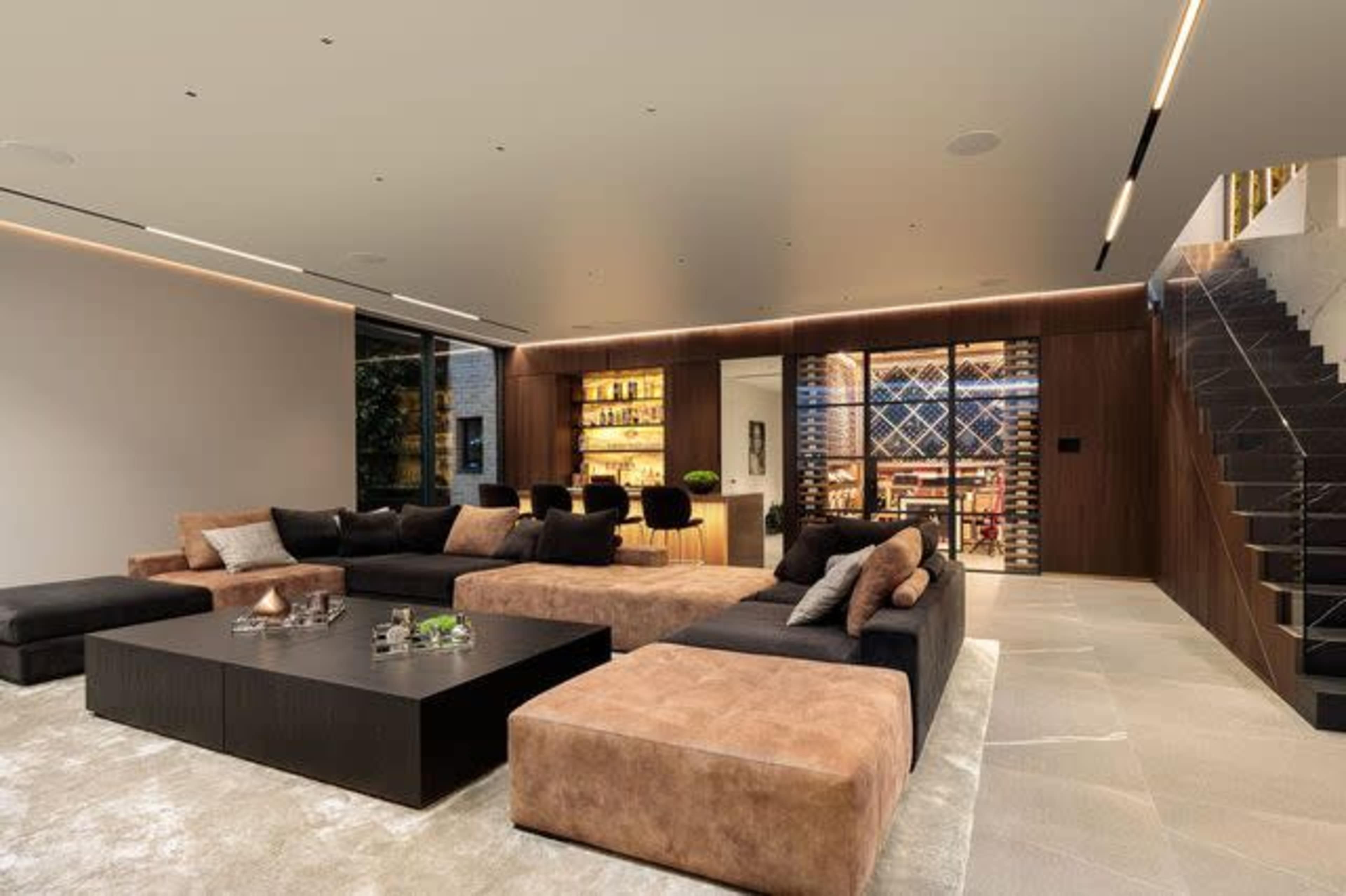 A modern living room with large sectional sofas, a low coffee table, and a staircase leading to an upper level.