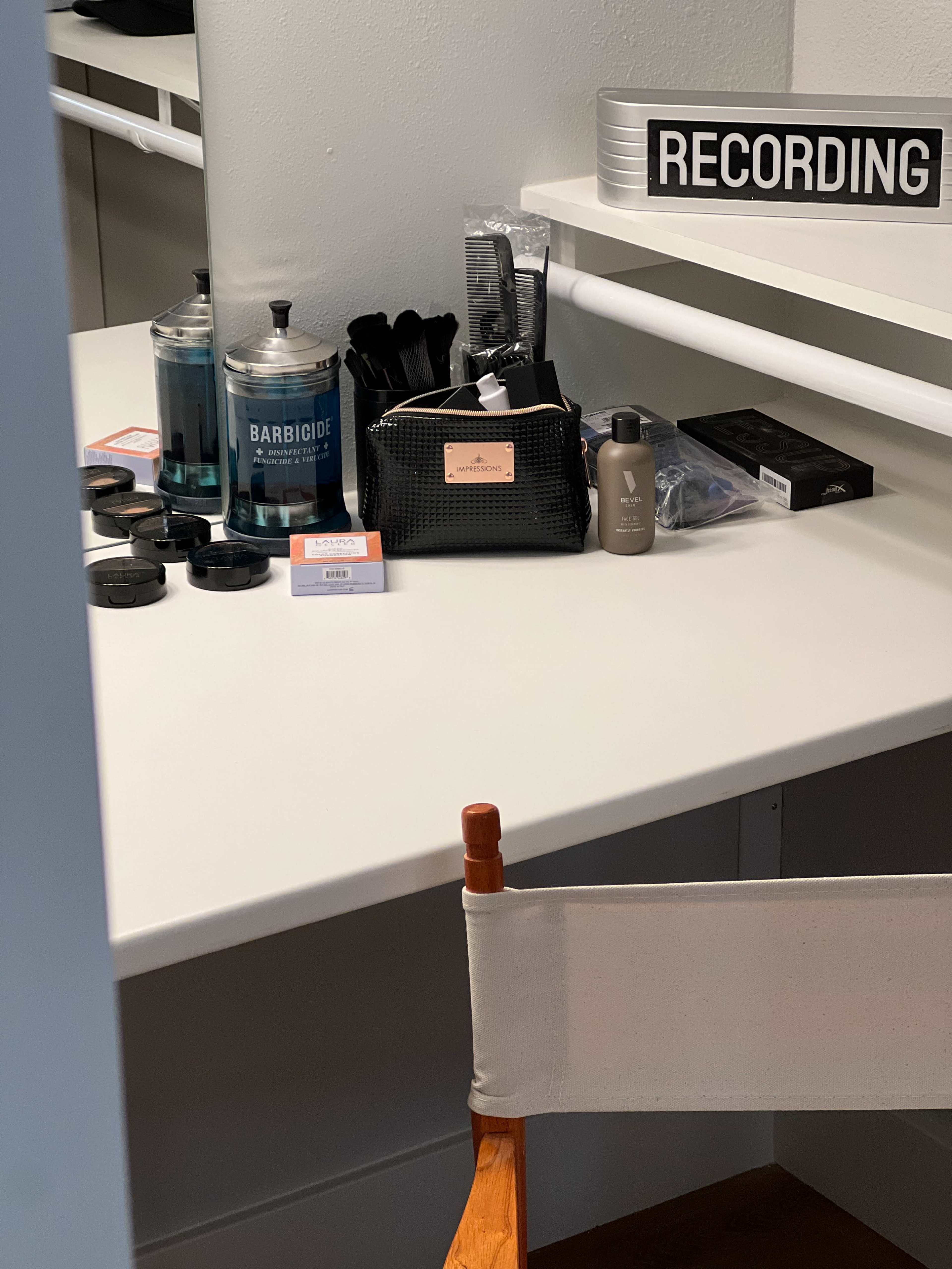 A makeup and grooming station featuring various products, tools, and a sign that reads "RECORDING."