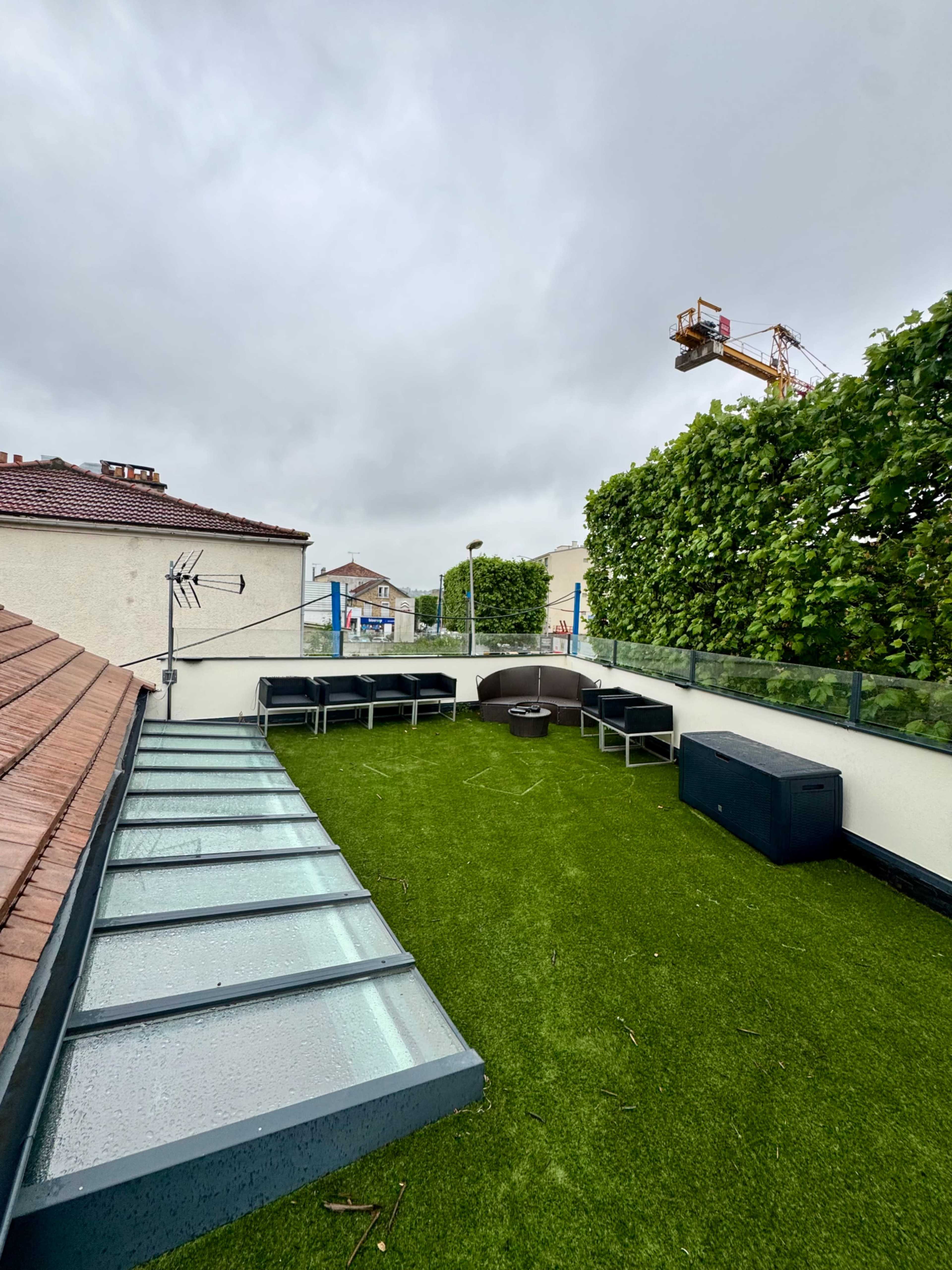 The image shows a rooftop space featuring artificial grass, seating arrangements, and a construction crane visible in the background.